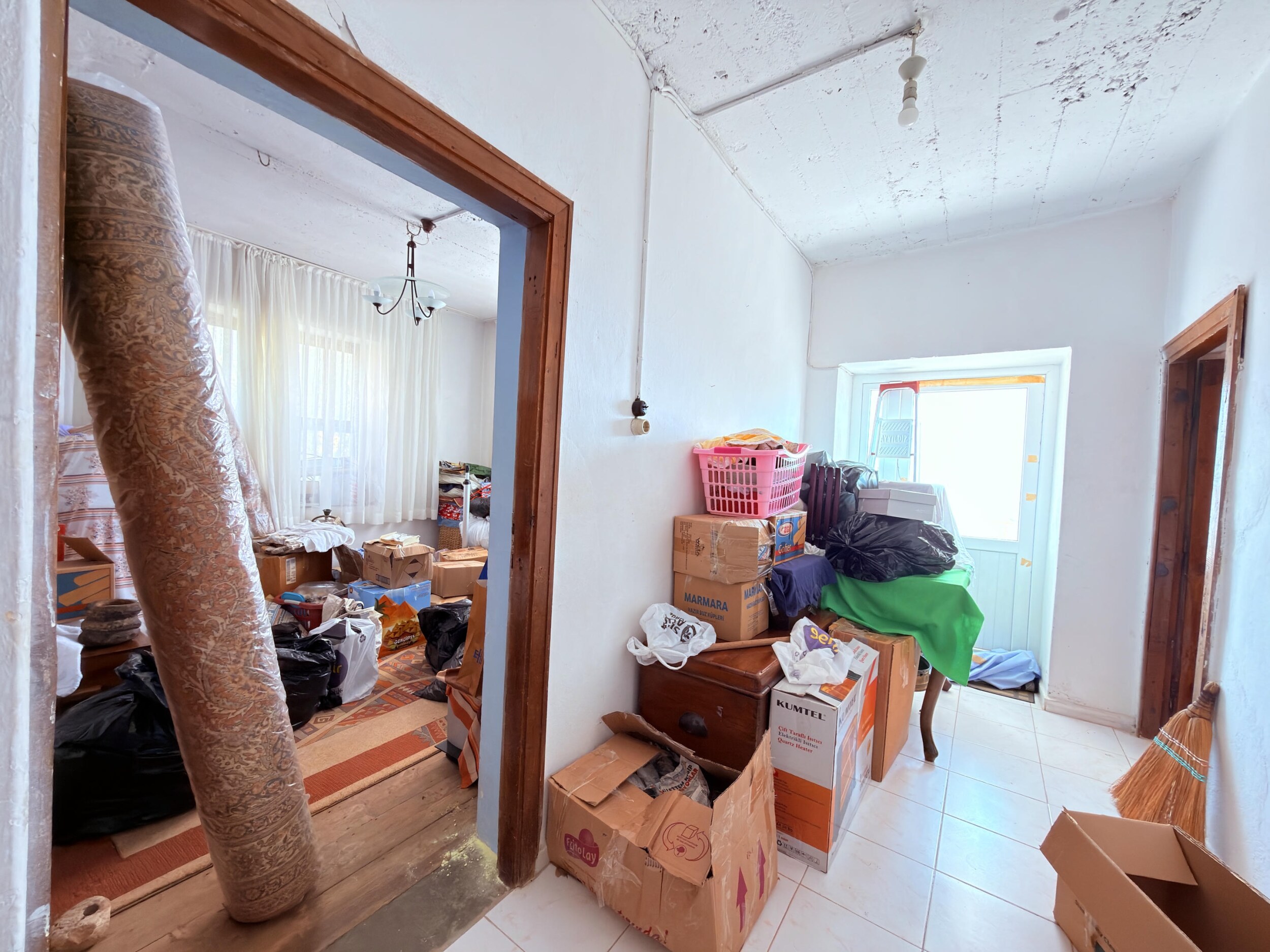 A white tiled corridor with doorways, boxes and a rolled carpet