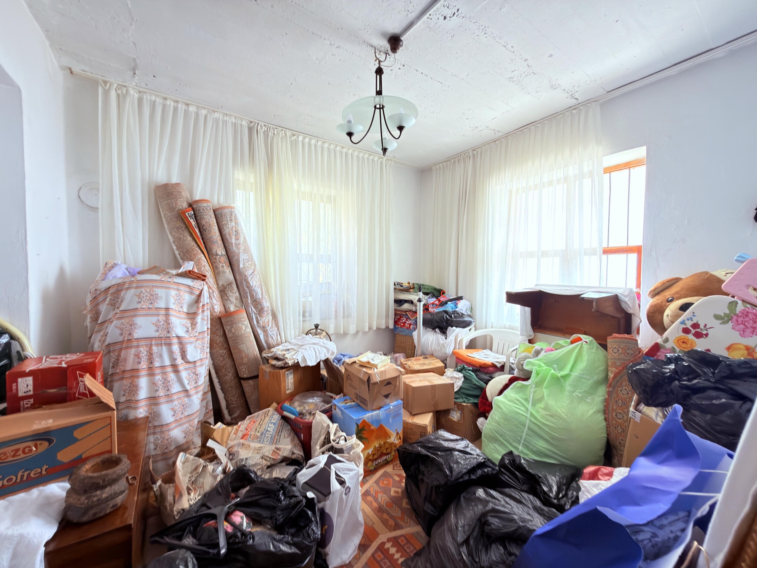 A villa room with corner glazing, sheer curtains, chandelier and scattered boxes in Alanya, Turkey