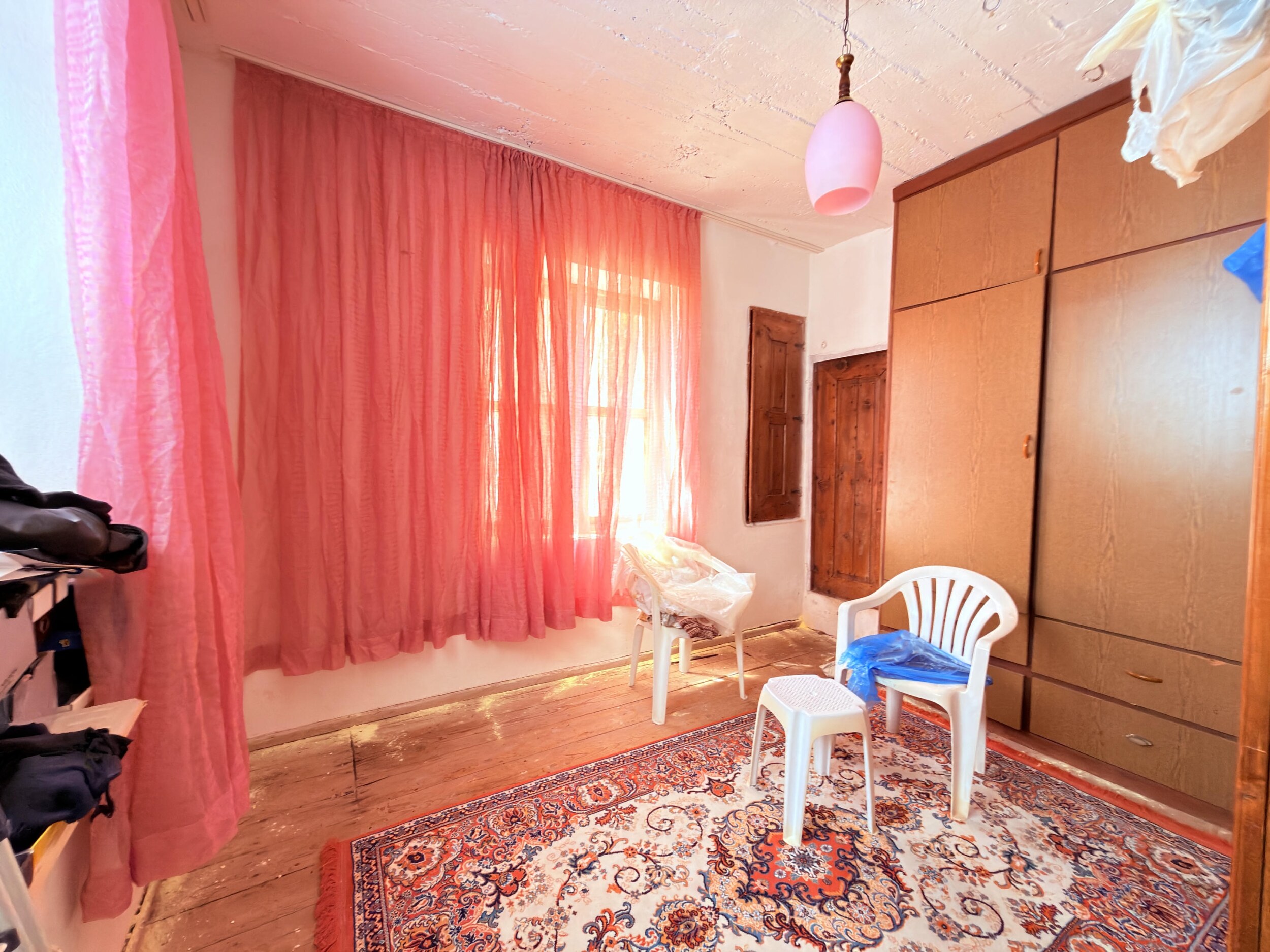 A room with wooden flooring, built-in wardrobe, red curtains and patterned rug in a villa