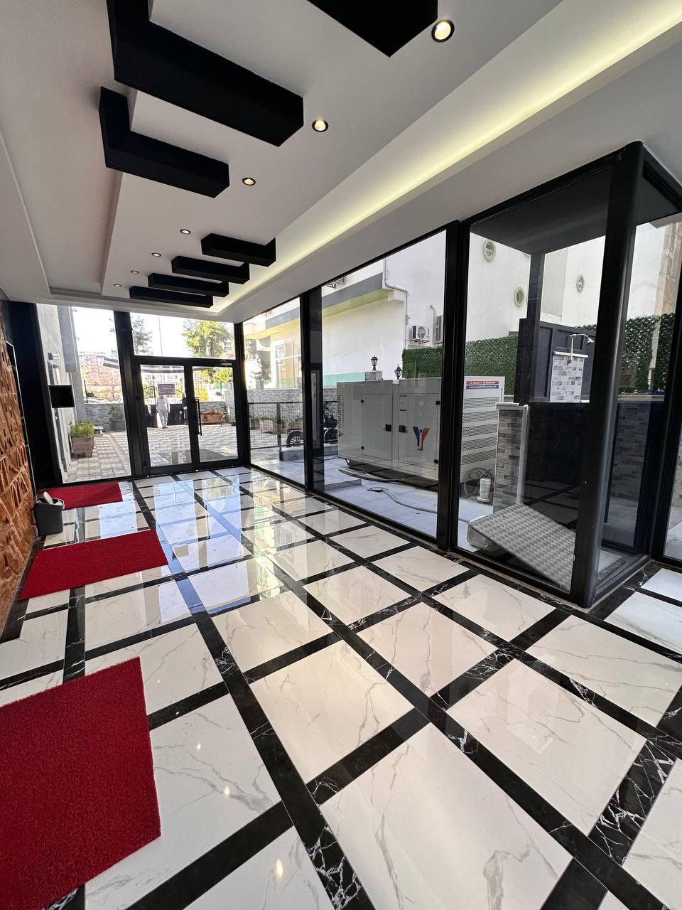 Parlak mermer zeminli giriş lobisi, dairelerin satışta olduğu binada cam kapı ve resepsiyon alanıyla