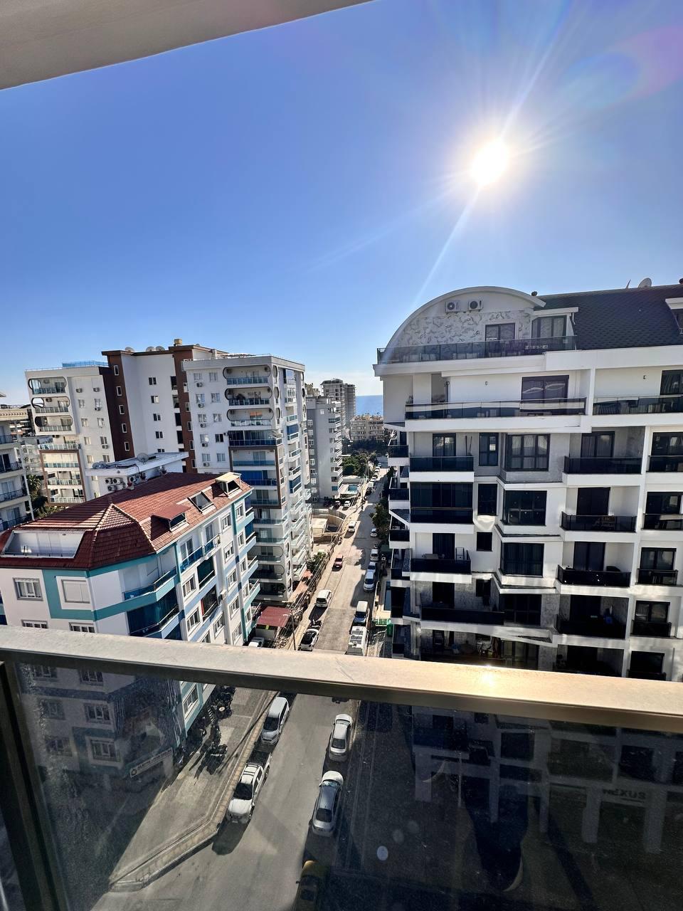 Balkon korkuluğunun ardında şehir sokağı, penthouse çevresindeki çok katlı binalar ve açık gökyüzü görünüyor