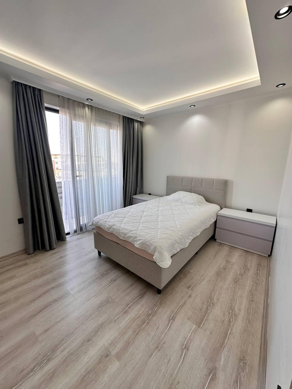 Gri yumuşak başlıklı çift kişilik yatak, penthouse yatak odasında panoramik pencere ve açık ahşap zemin yanında
