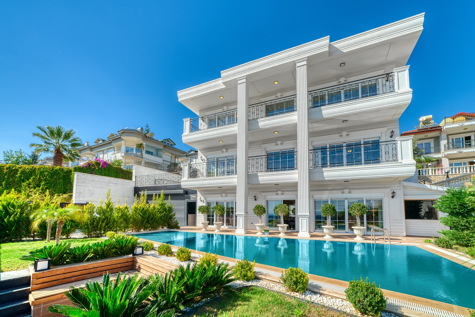 Three-story white villa facade with a pool and palms presents a 5+1 villa for sale in Alanya, Turkey — New Level Group