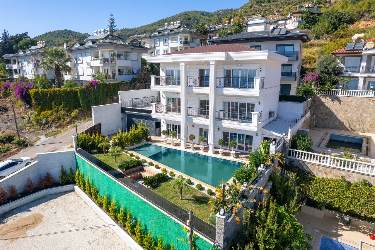 A villa with a pool on a fenced plot among hills and neighboring apartment buildings in Alanya for sale