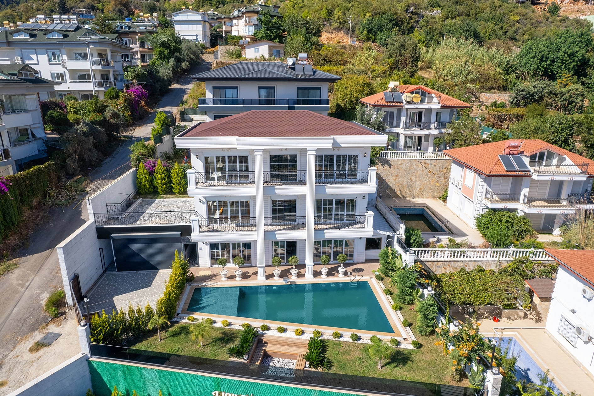 Villa facade with a pool and red-brown pitched roof on a green hillside plot in Turkey for sale