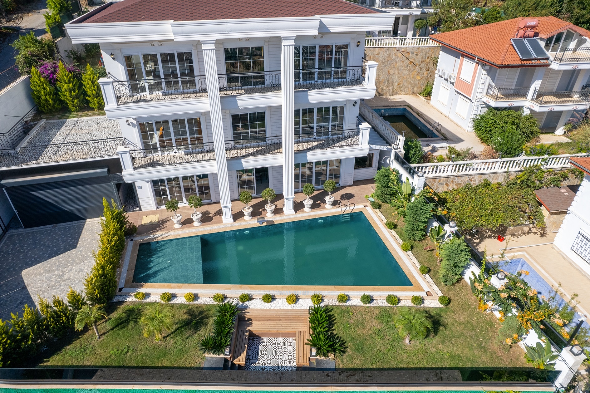 Rectangular pool before a three-story villa facade with balconies and a lawn in Alanya, Turkey