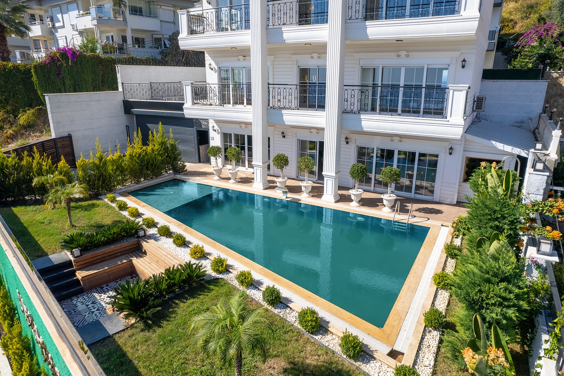 Pool beside a villa facade with panoramic windows and a wooden garden seating area in Turkey for sale