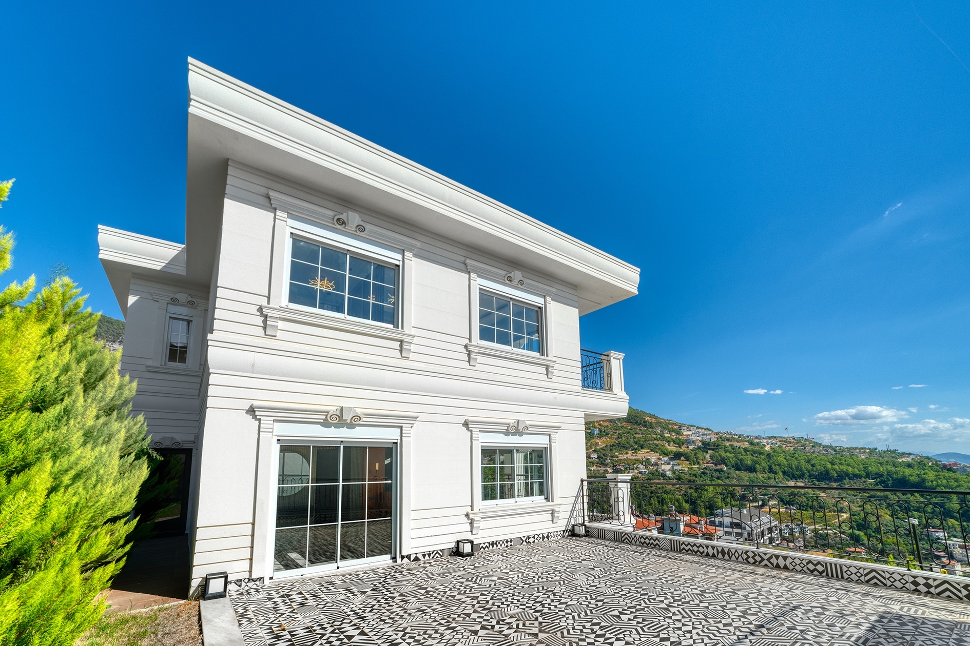Spacious villa terrace with black-and-white tiles, panoramic windows and a green mountain slope in Alanya for sale