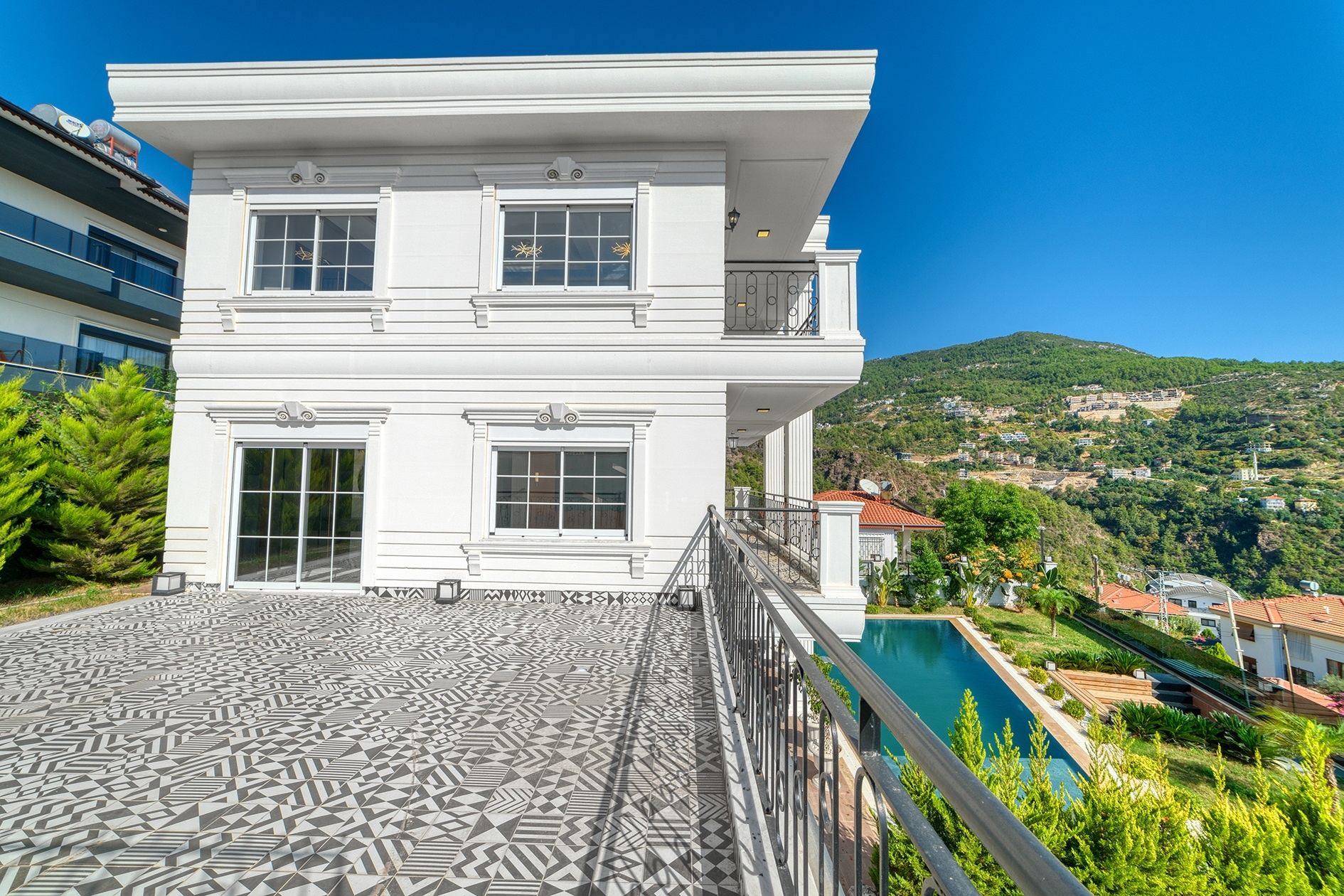 Large villa terrace with patterned tiles, a pool and a green mountain slope in Turkey for sale