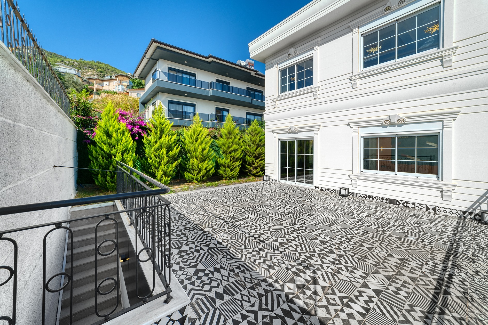 Villa terrace with spiral metal railings, steps and bougainvillea beside a white facade in Alanya, Turkey