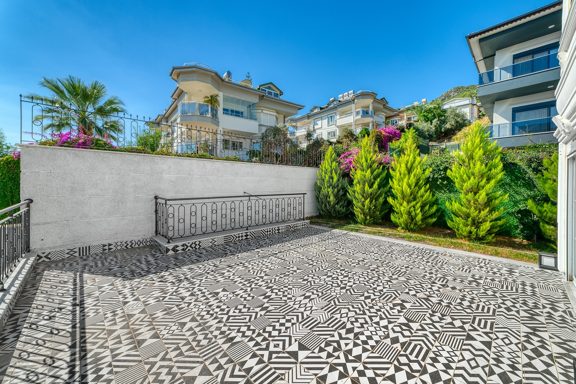 Spacious villa terrace with patterned paving, shrubs and a stone retaining wall in Turkey for sale
