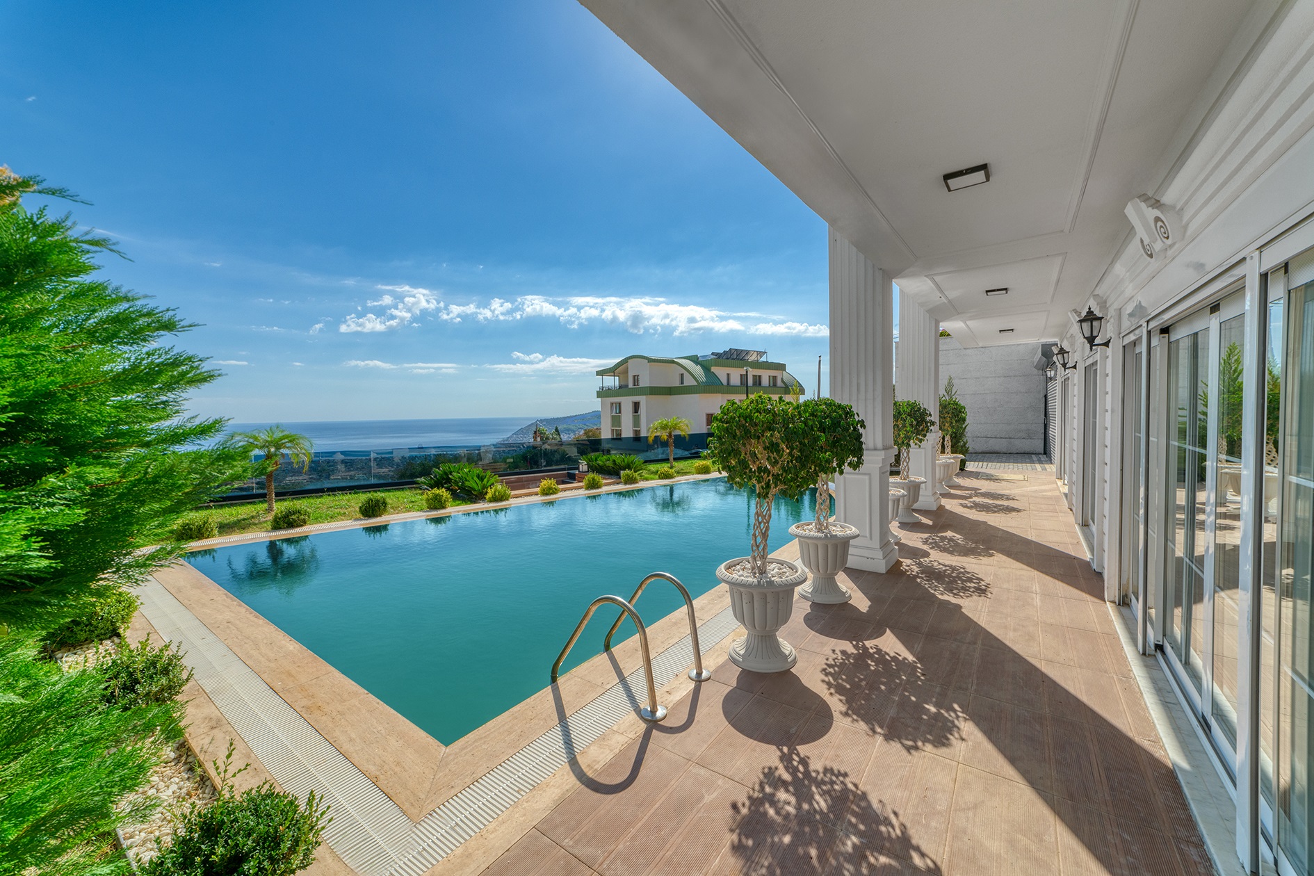 Open pool with a ladder beside a covered terrace overlooking the sea and mountains in Alanya, Turkey