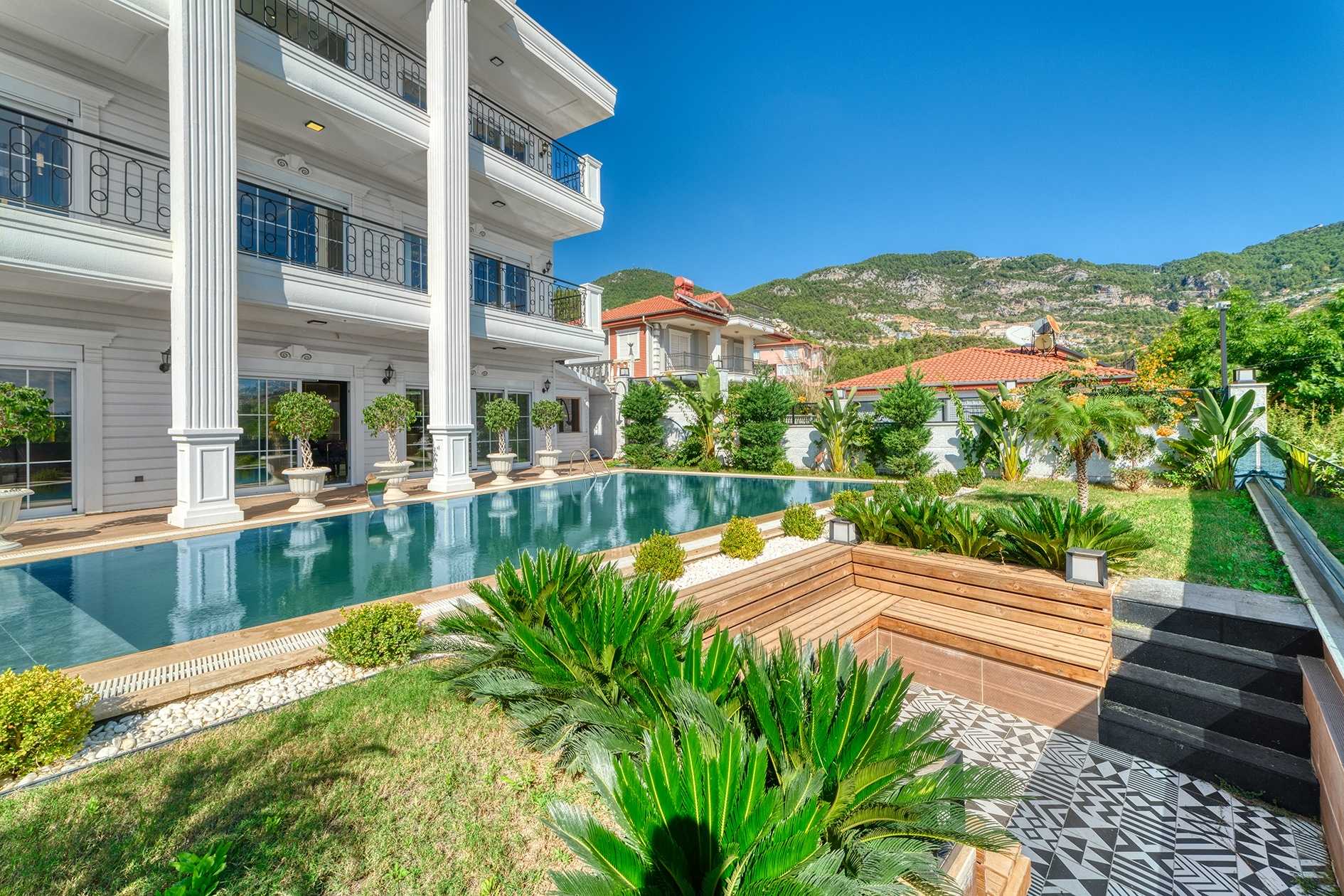 Long pool along a villa facade with a wooden seating area and mountain slope in Alanya for sale