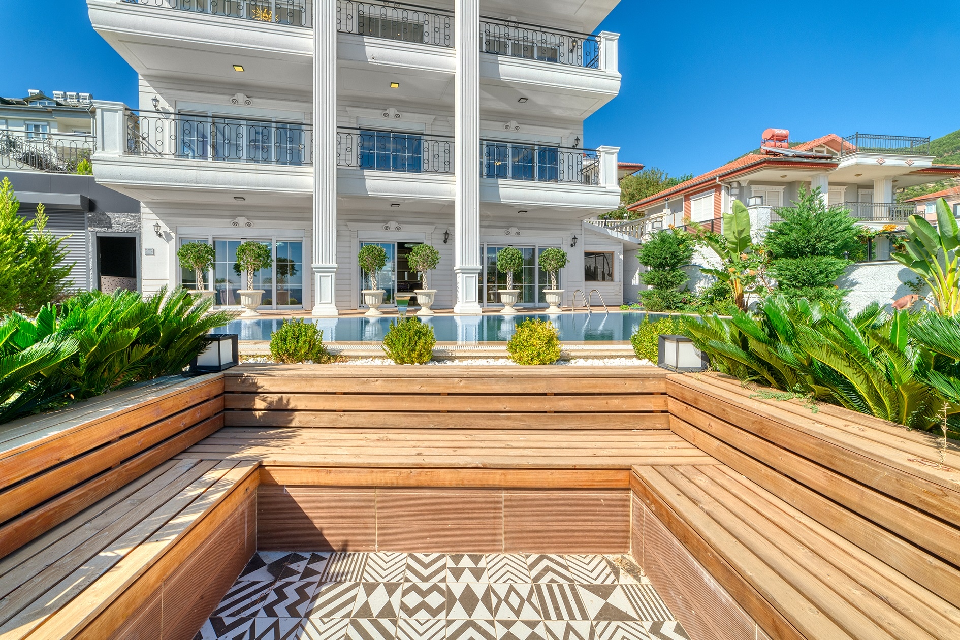 Tiered wooden seating area beside a pool before a white villa facade in Turkey for sale