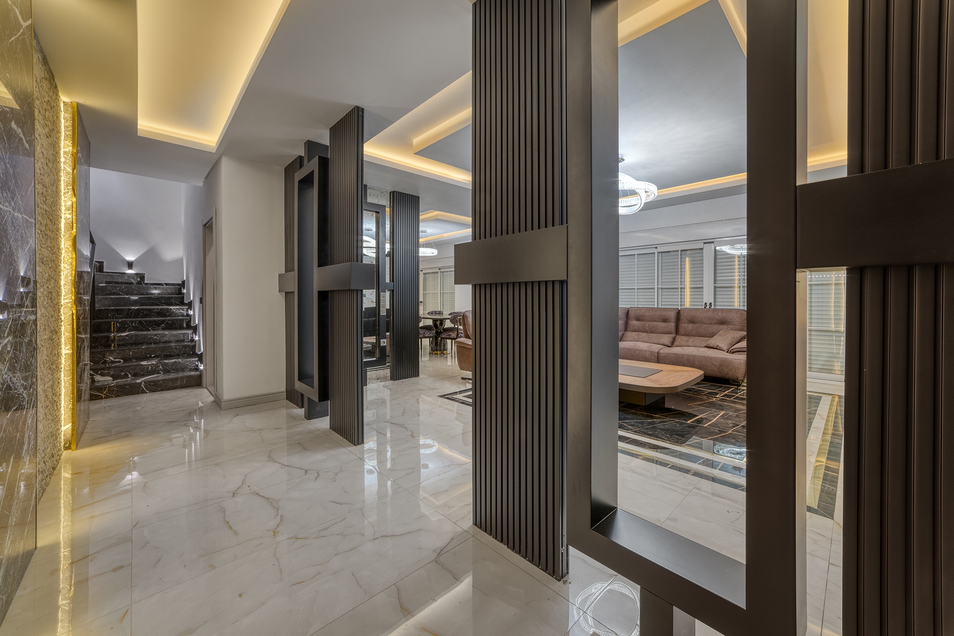 Bright villa hall with a black staircase, marble steps and a beige sofa in the living room