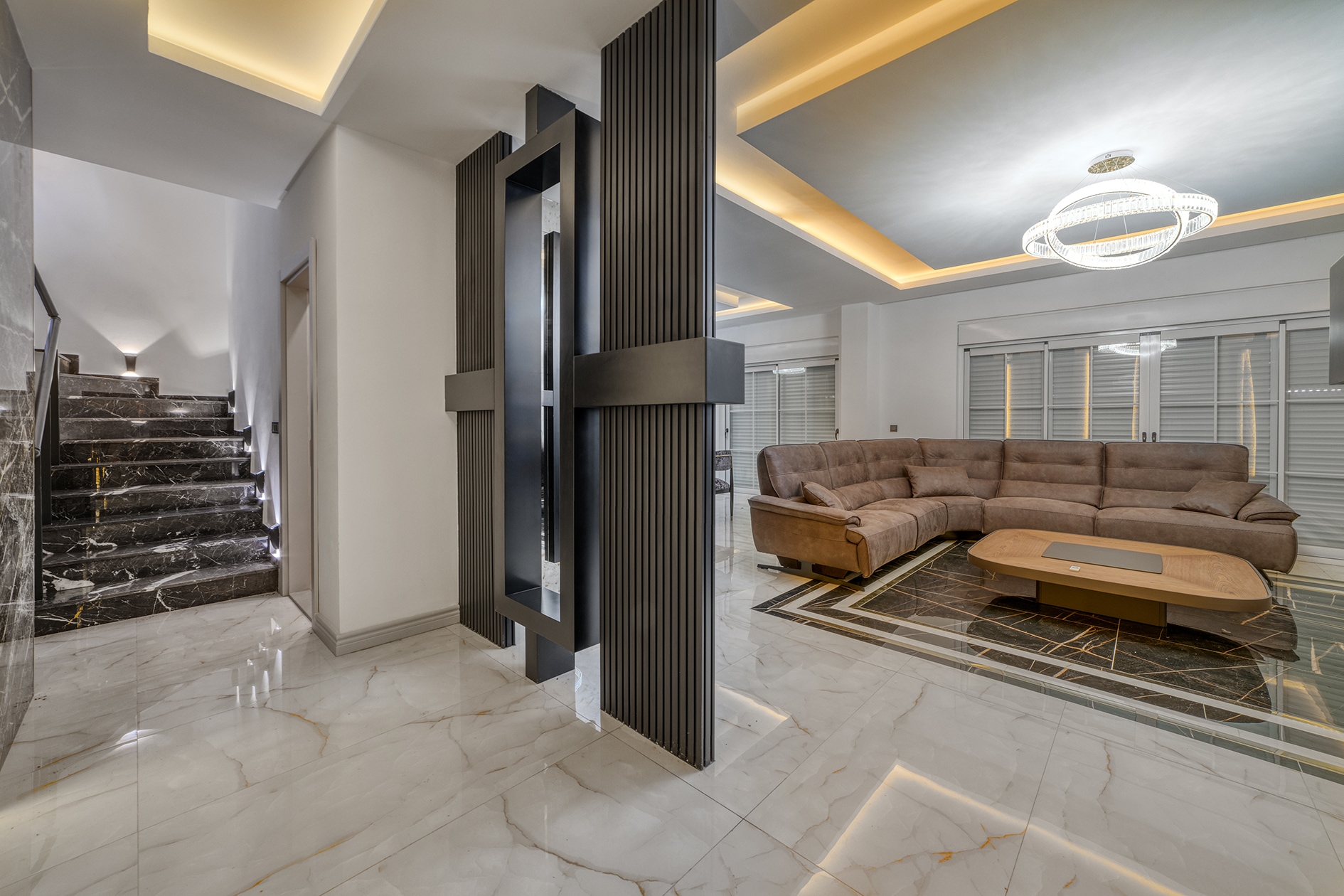 Villa living room with a brown corner sofa, oval table and dark marble staircase in Turkey for sale