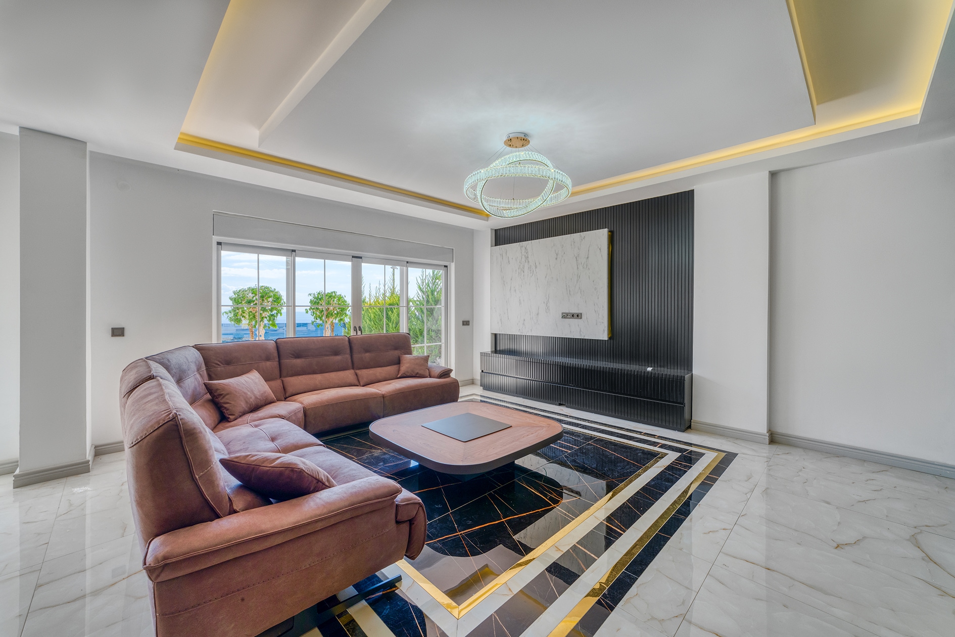 Villa living room with a brown sofa, panoramic glazing and greenery beyond the windows in Alanya for sale
