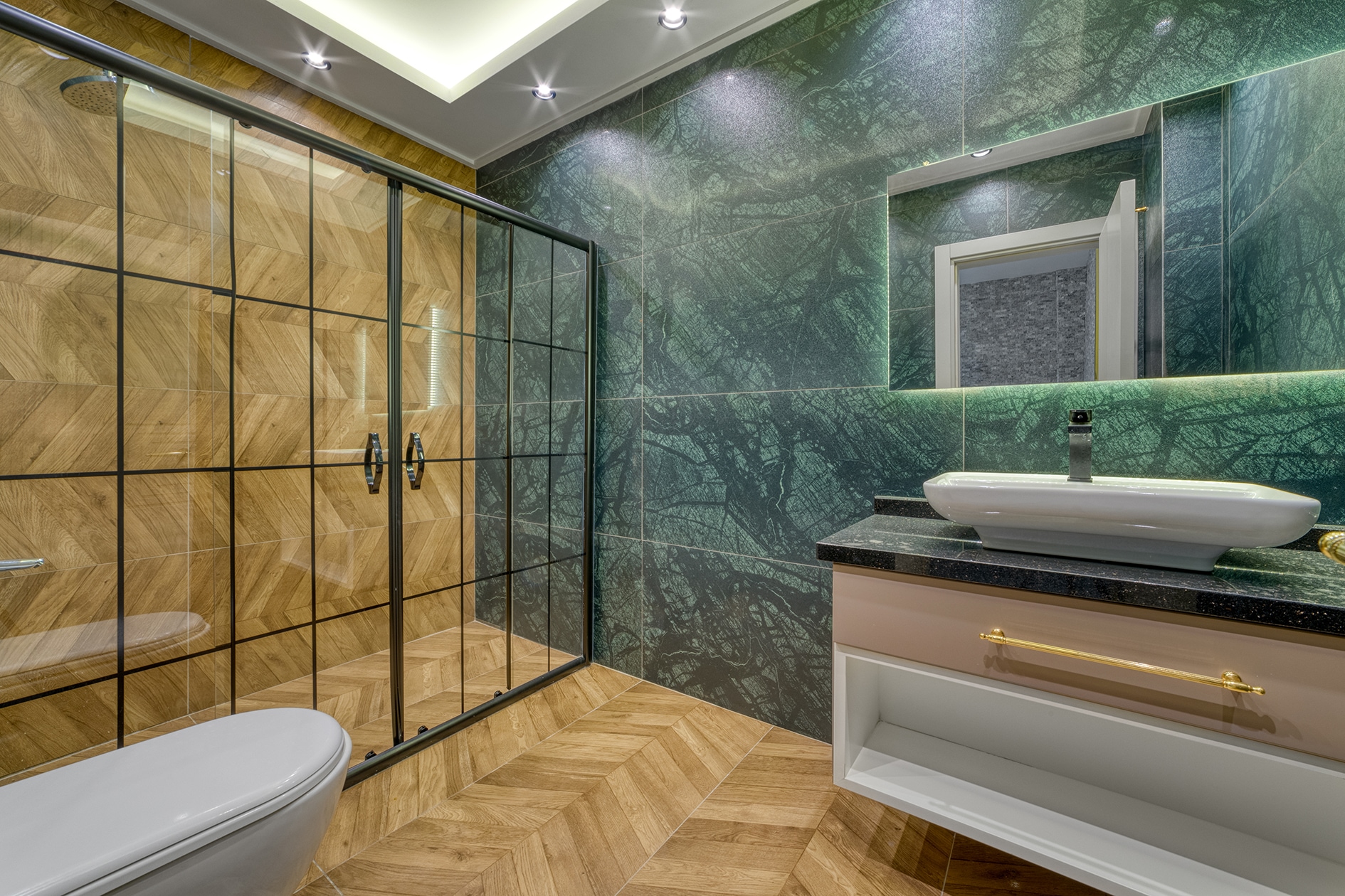House bathroom with glass shower, green marble walls and a gold-fitted basin in Alanya