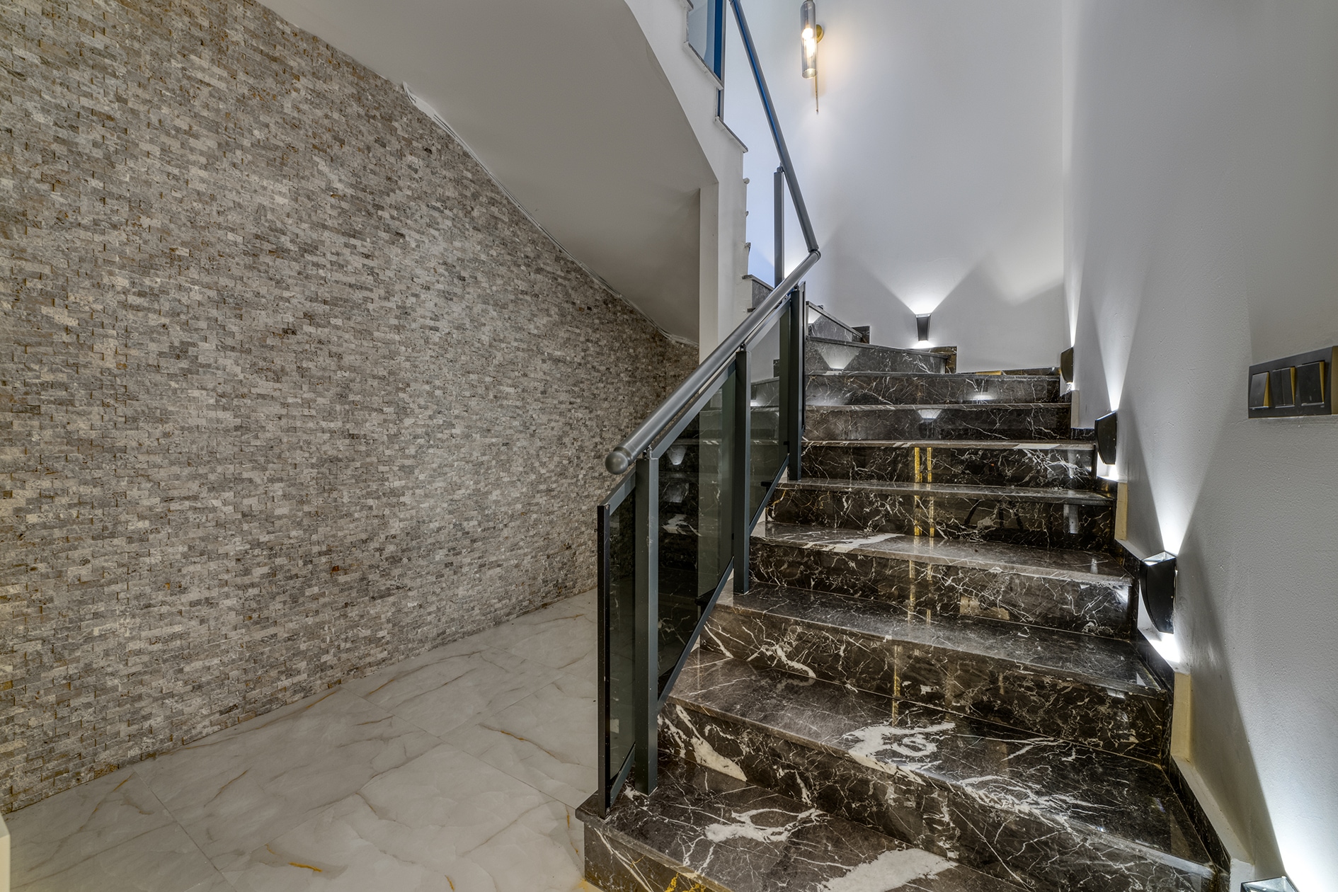 Staircase with black marble steps, glass balustrades and a ceiling light opening
