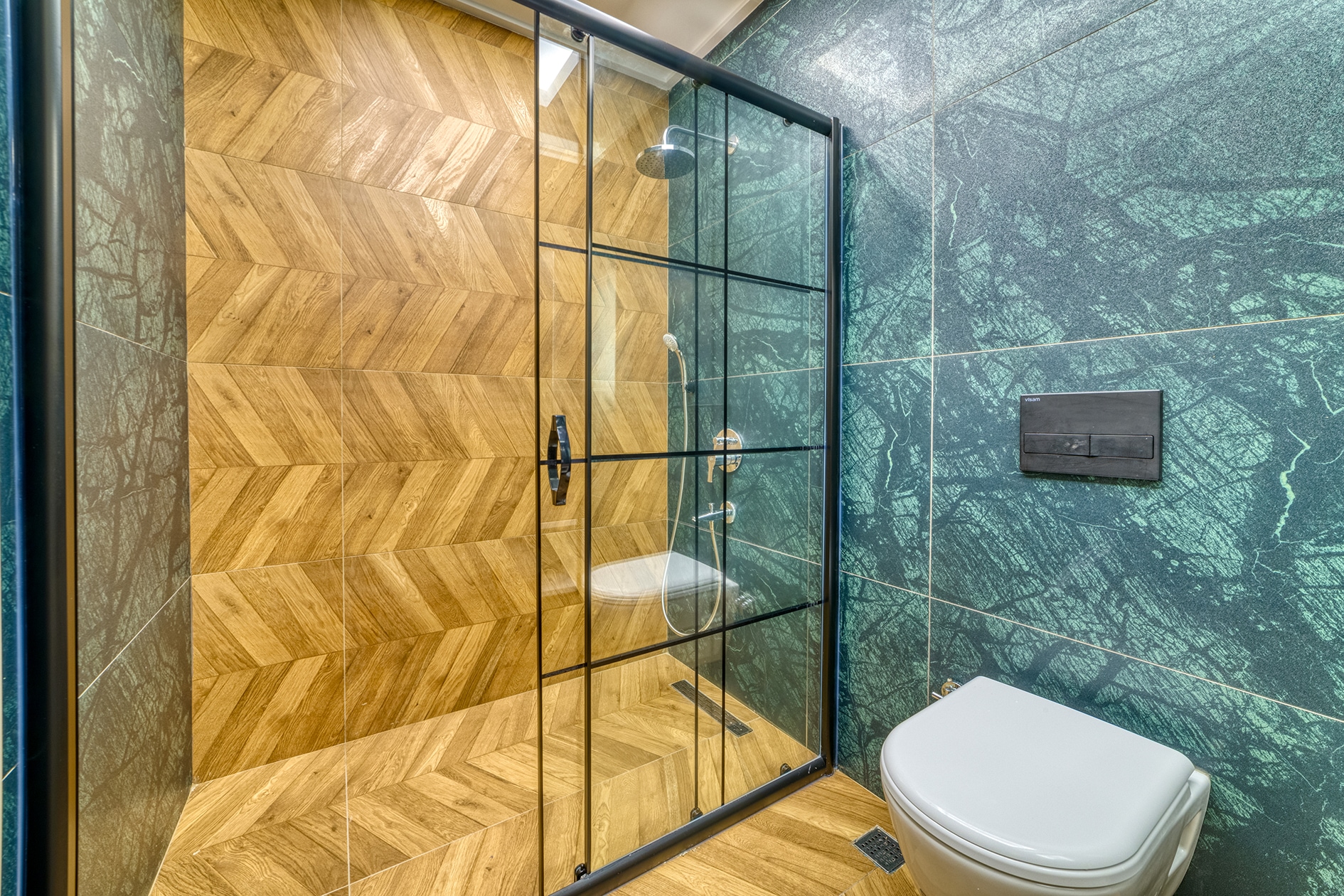 Glass shower enclosure with a black frame and dark green marble tile in a villa bathroom