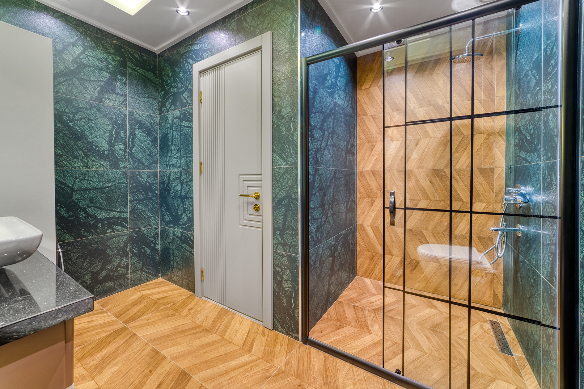 Glass shower enclosure with green patterned tile and a dark countertop basin