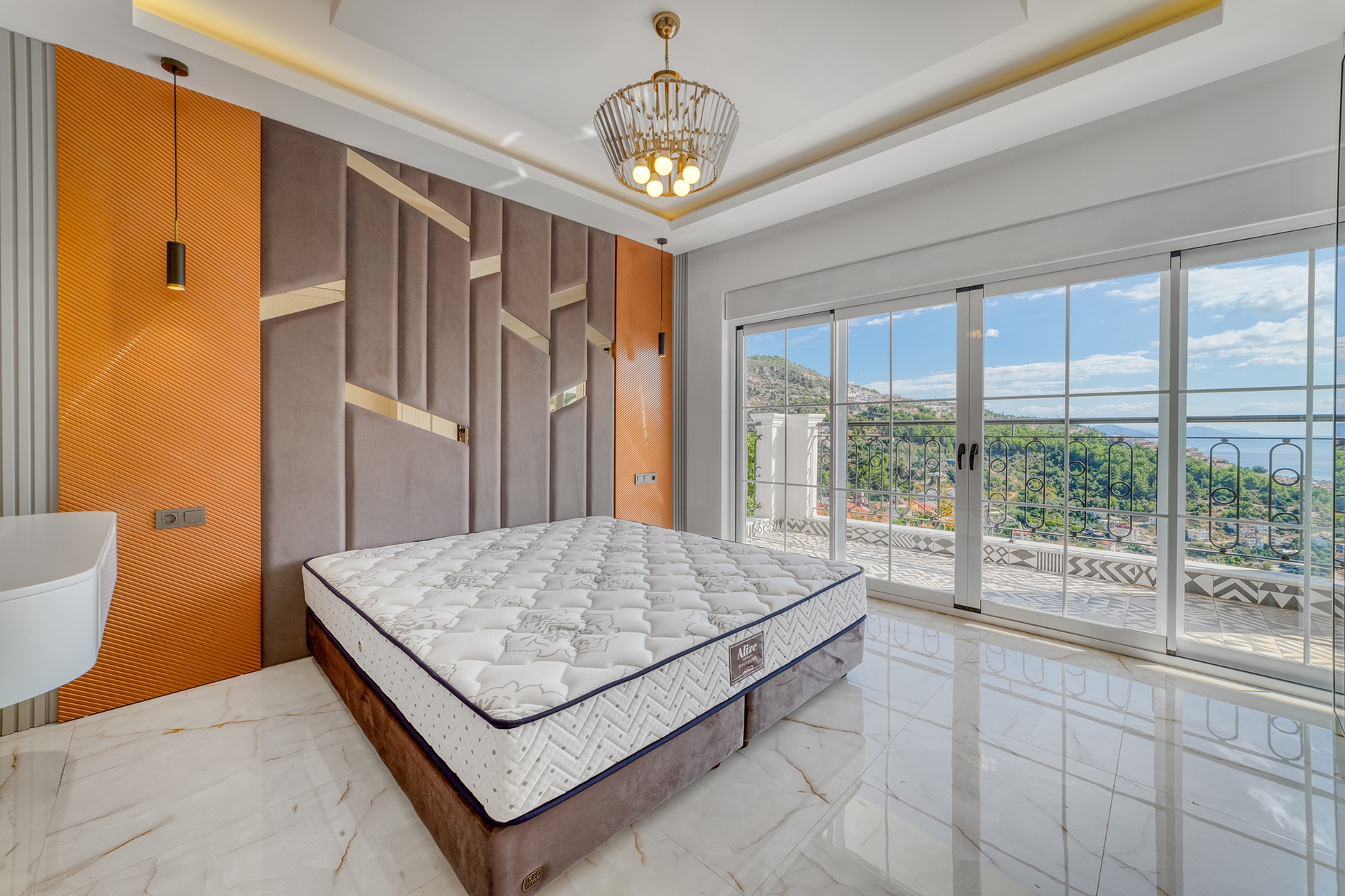 Double bed beside panoramic balcony doors with sea and green slope views