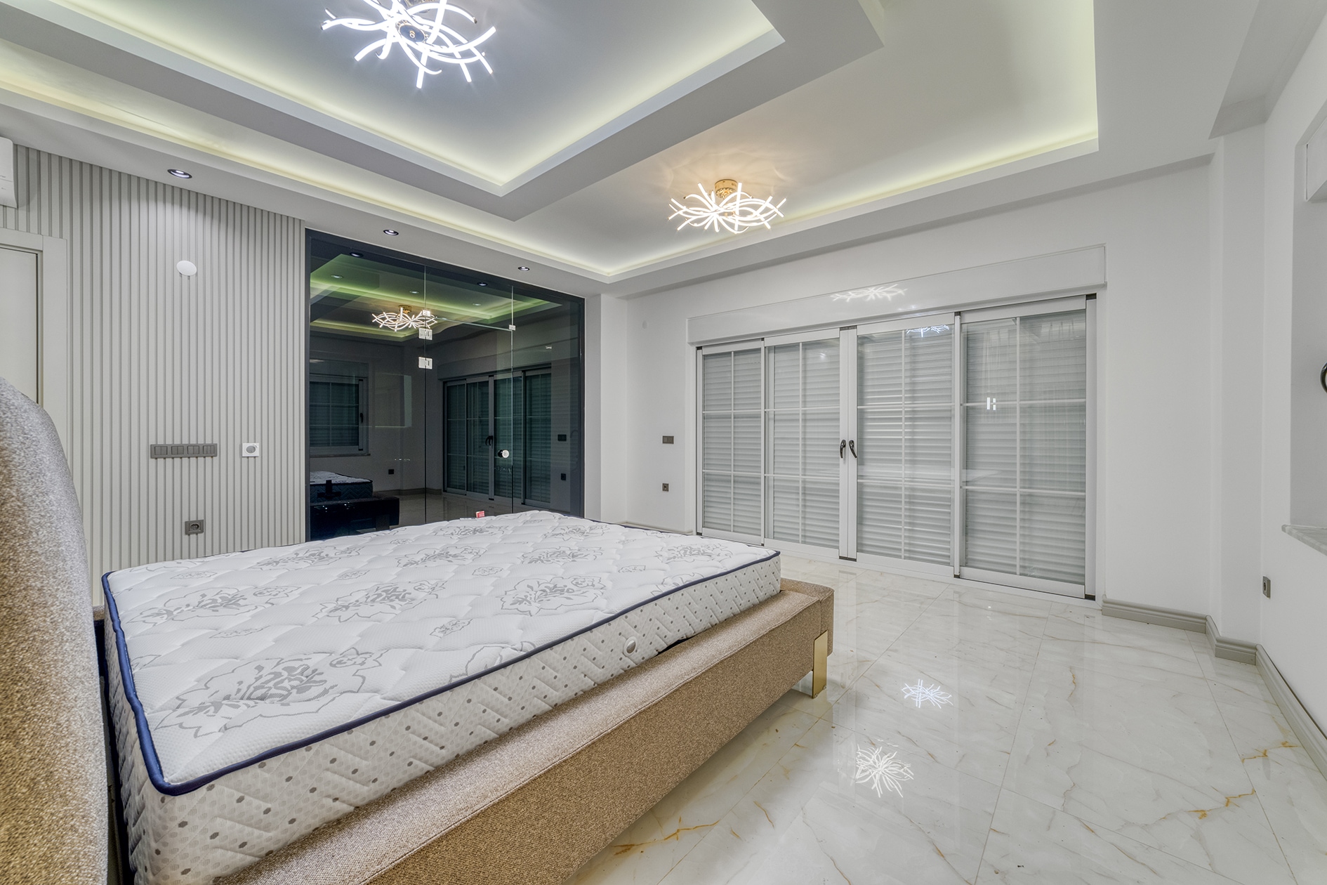 Beige bed beside panoramic doors and a gray-white slatted wall panel