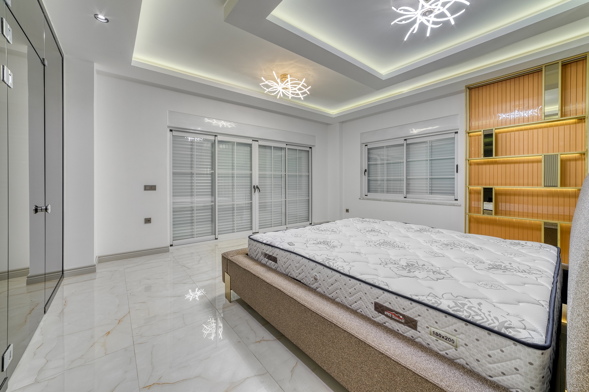 Bed with white mattress and mirrored wardrobe beside a panoramic door in a villa bedroom