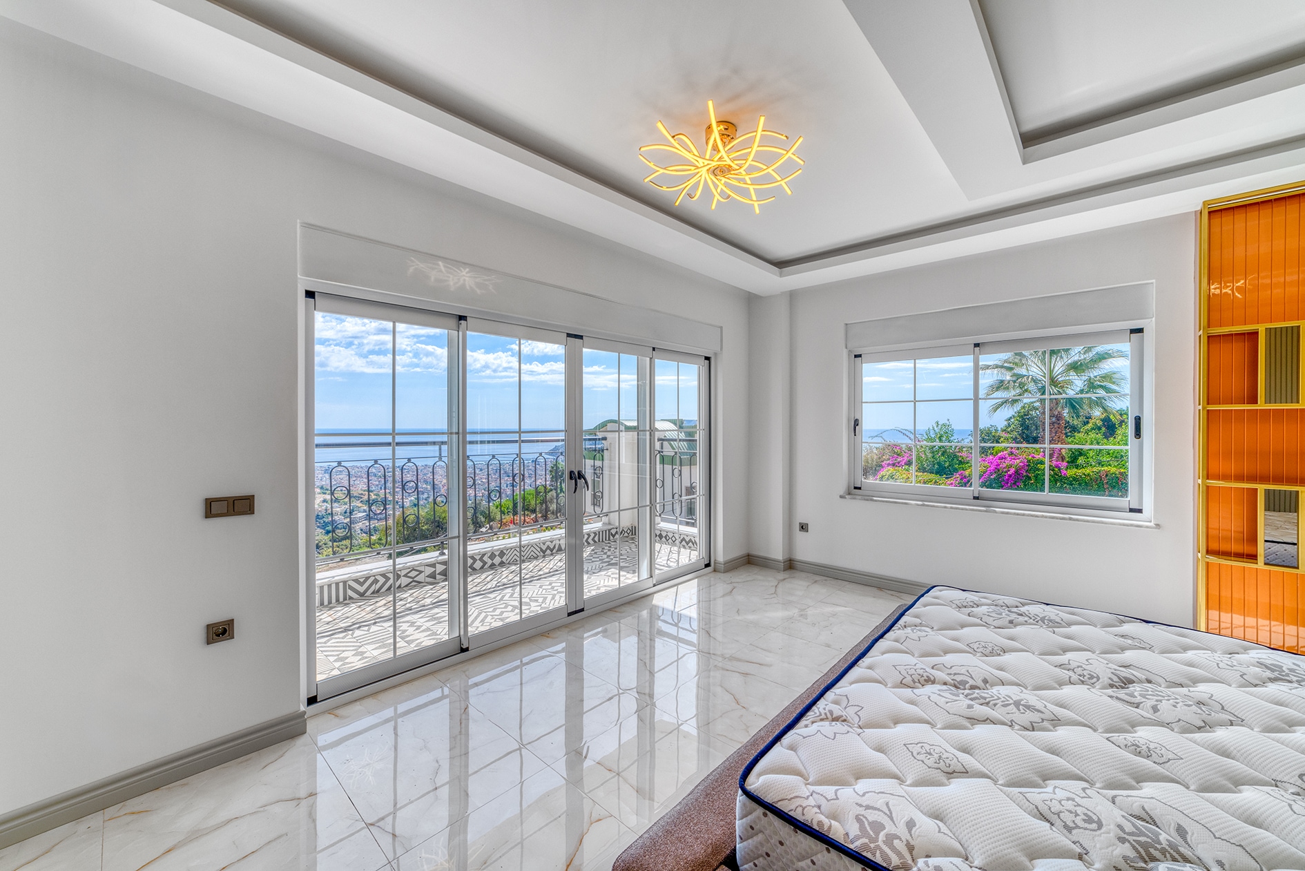 Bed with white mattress and corner window opening to the outside in a villa bedroom