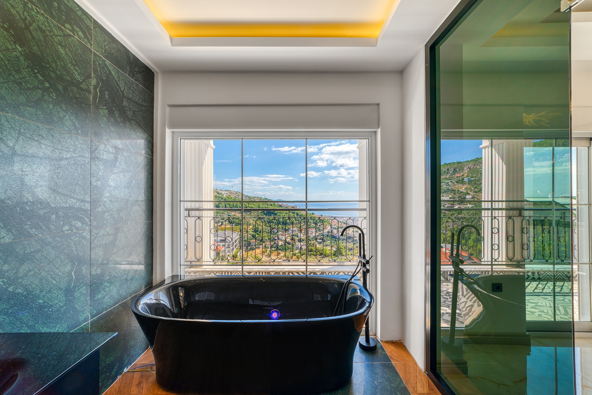 Black bathtub by a window with mountain slope and sea views in a villa bathroom in Alanya