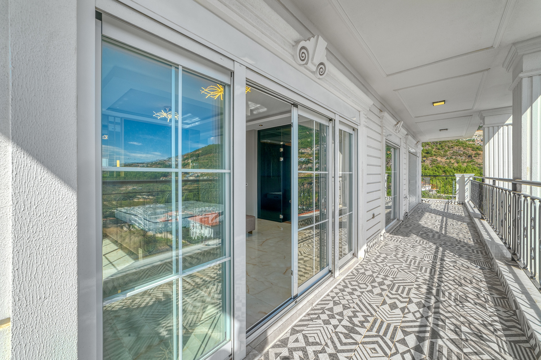 Covered terrace with black railings and views of a green mountain slope at a villa