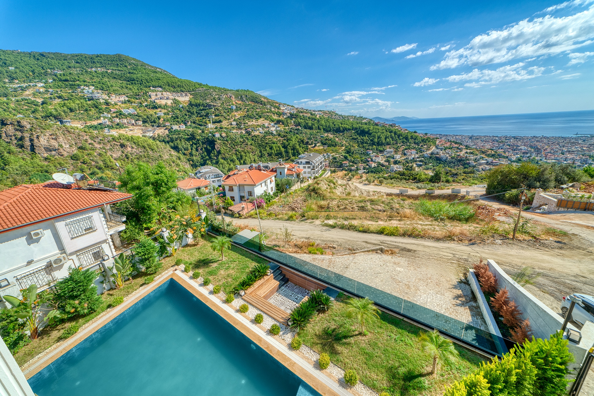 Outdoor pool corner with green garden and sea beyond beside a house for sale