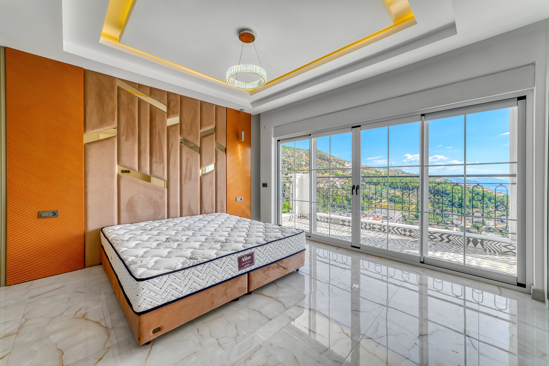 Double bed beside an orange wall and balcony with metal railing in a villa bedroom