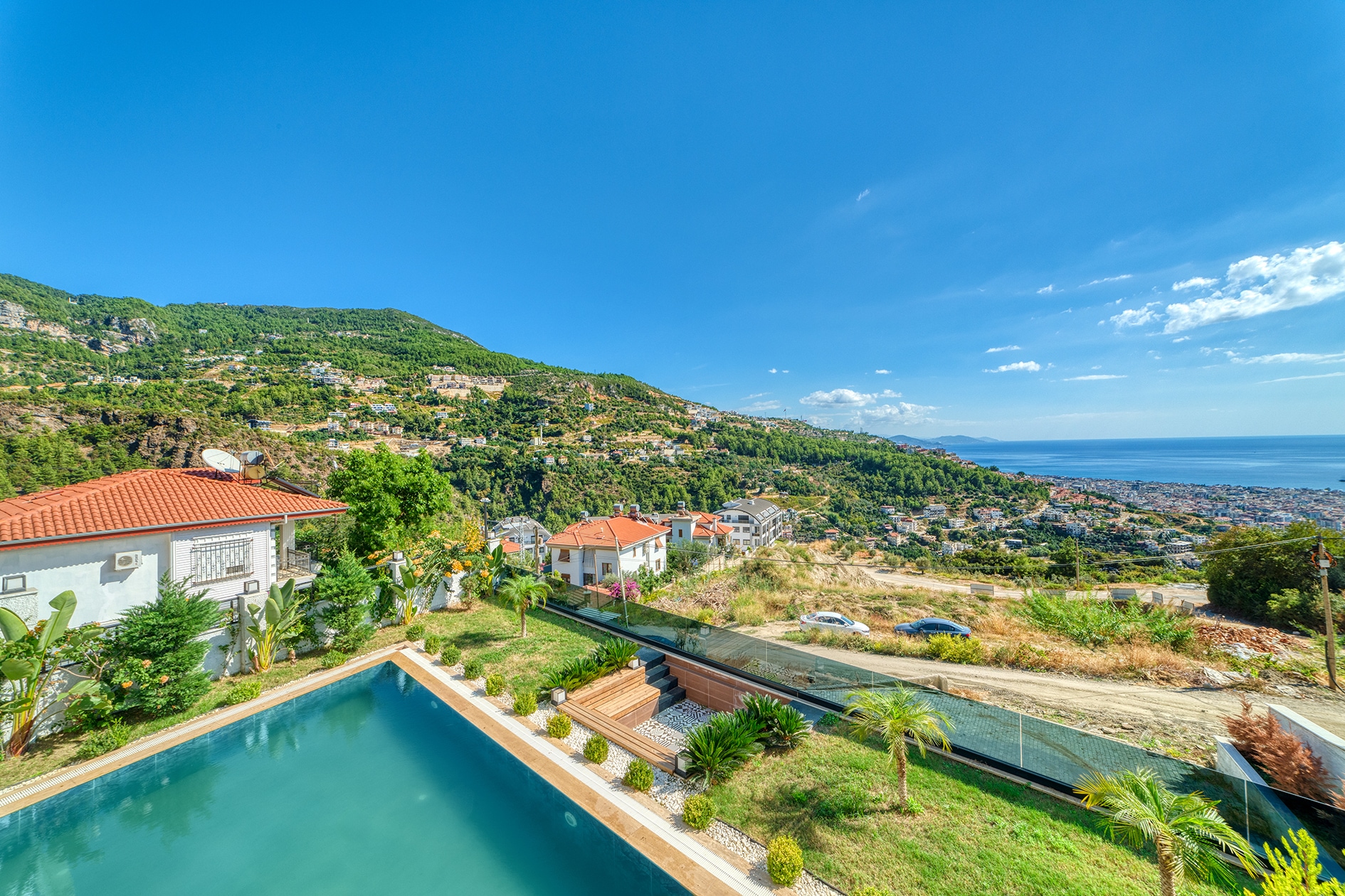 Outdoor pool with lawn, palms and sea views beside a house in Alanya