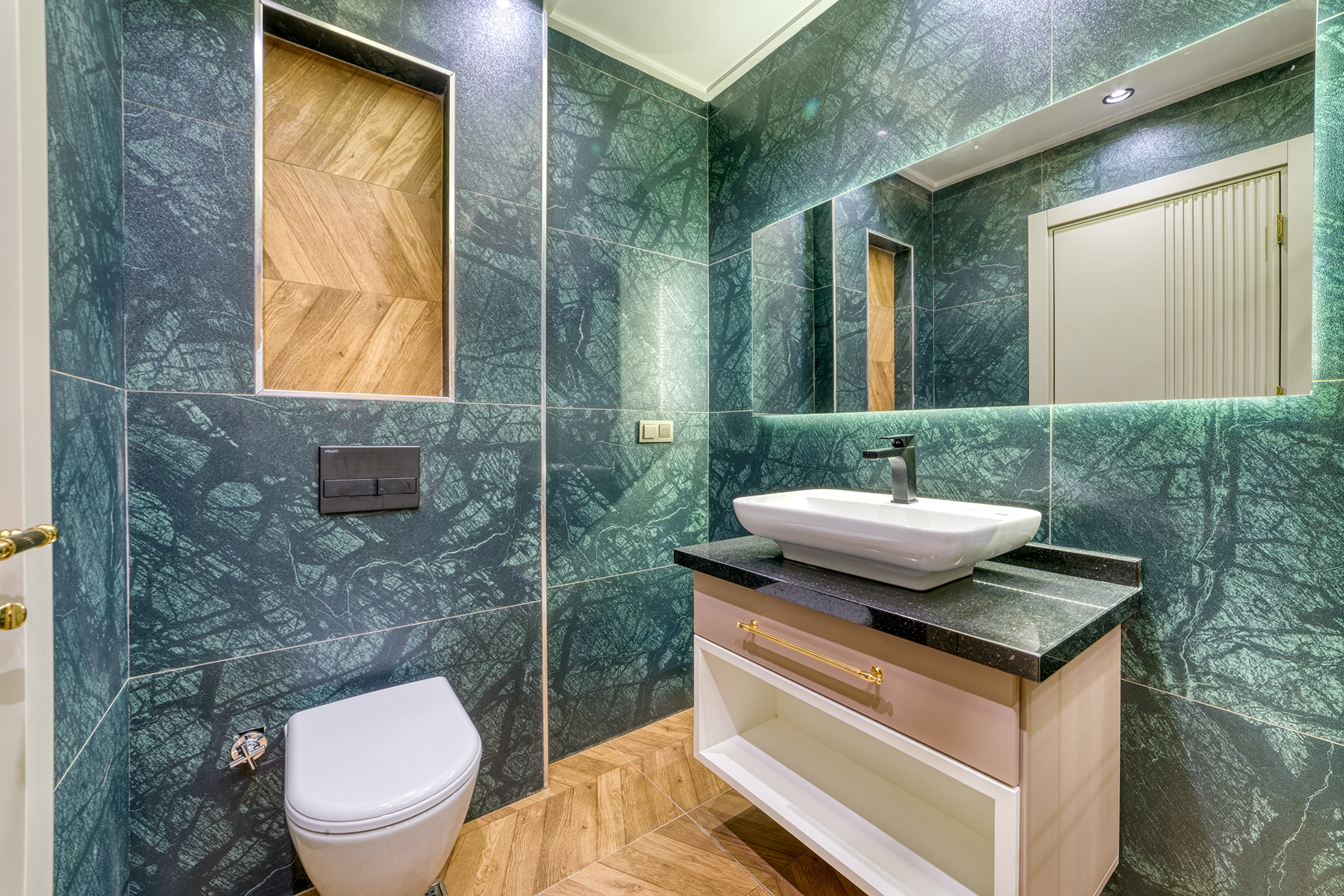 White basin on a black stone counter with textured green tile in a bathroom in Alanya