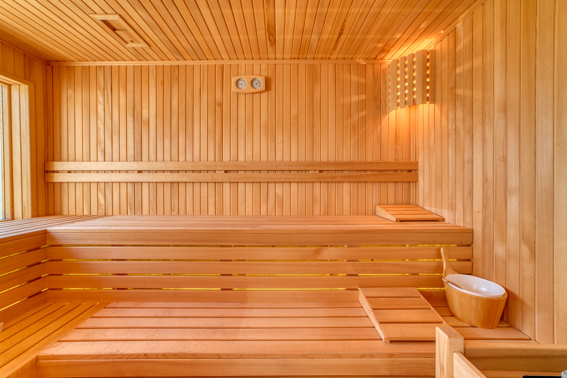 Sauna with tiered wooden benches, warm wall lighting and a wooden bucket in Alanya