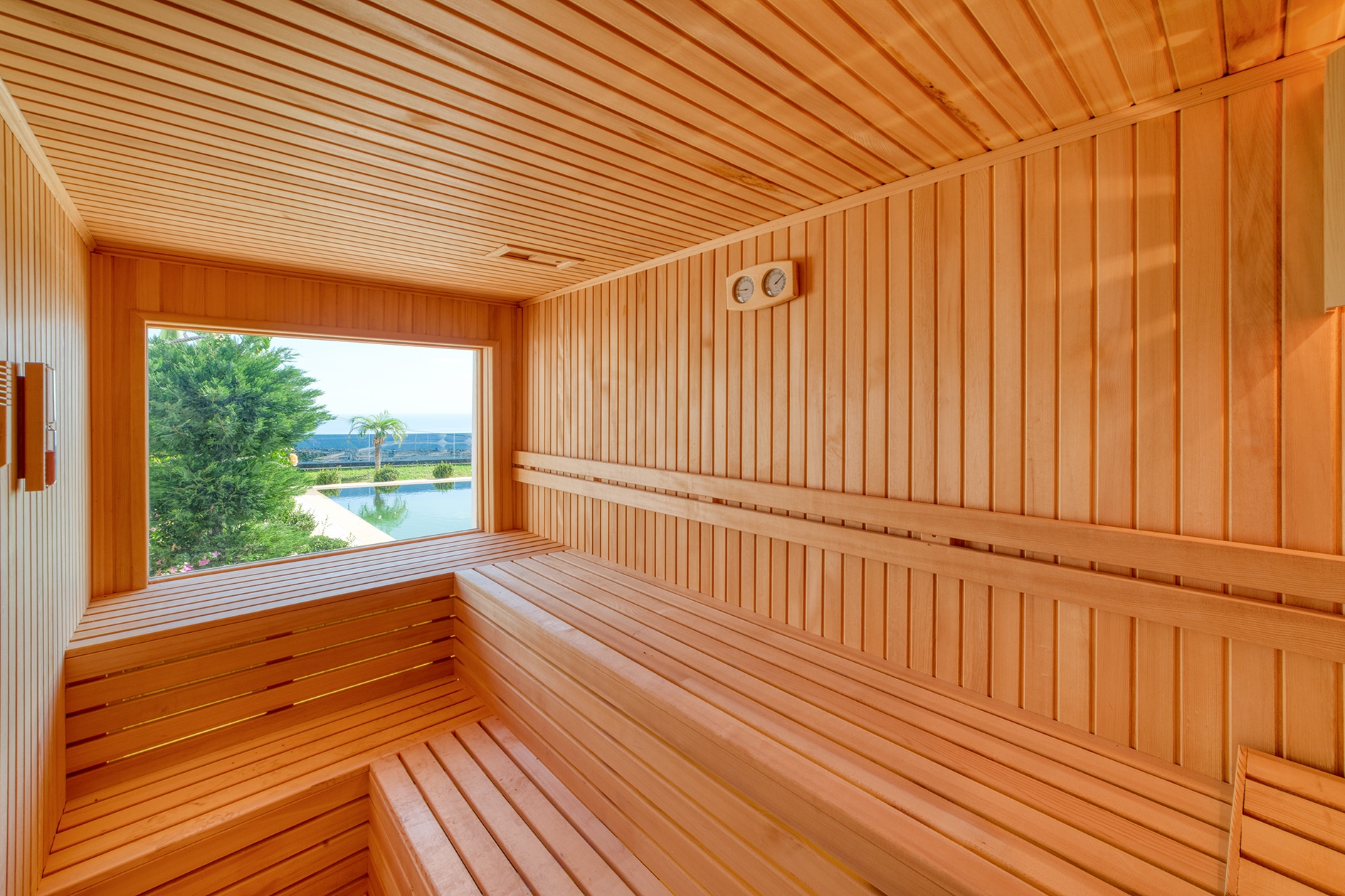 Panoramic-window sauna with tiered wooden benches and garden greenery for residents of villas