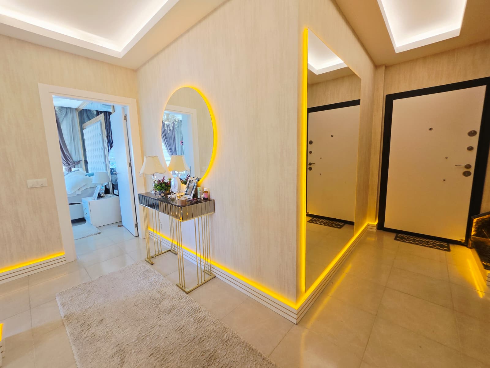 Açık renk giriş kapısı, oval aynalı konsol ve bej halı penthouse koridorunda