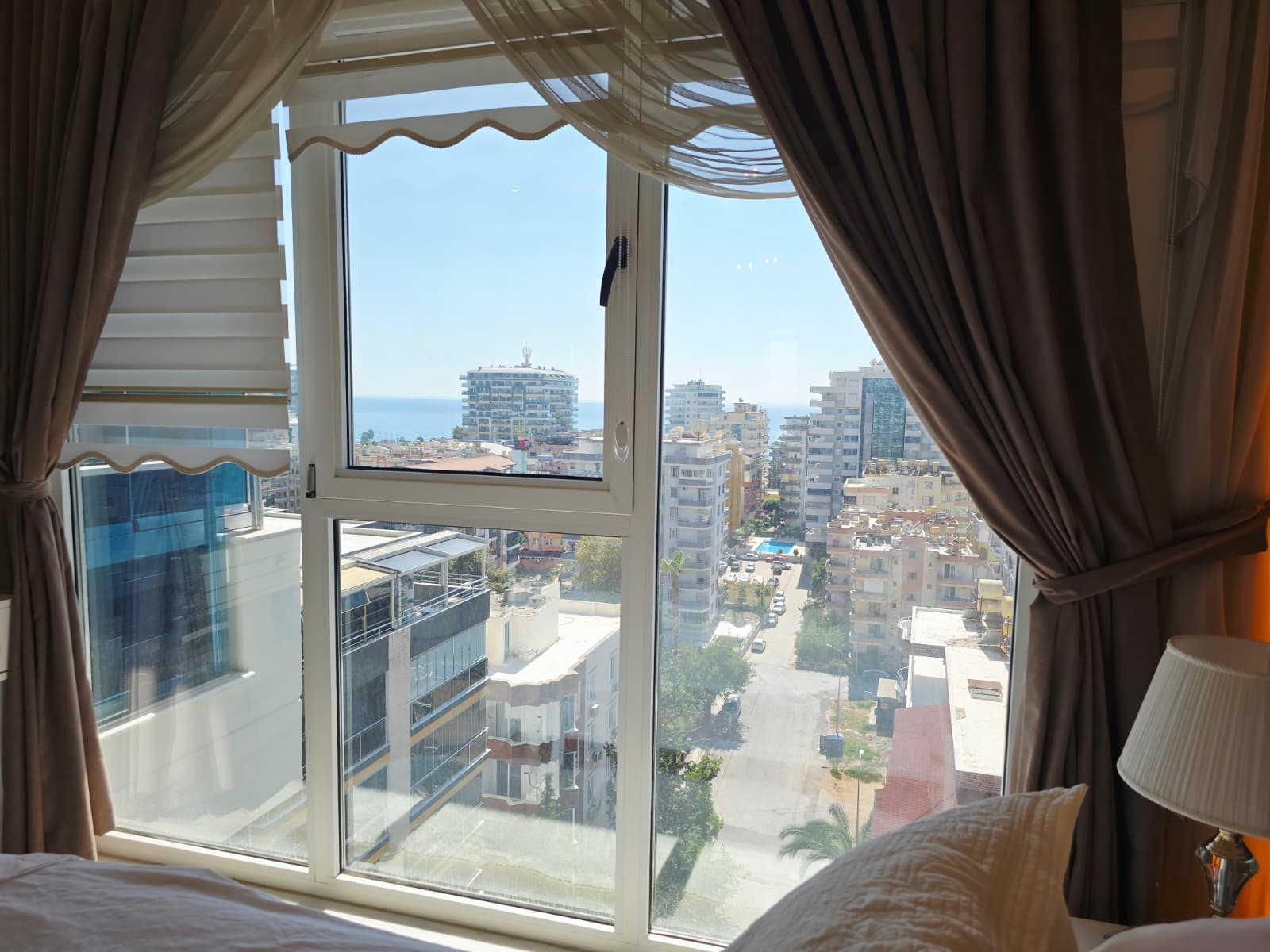 Şehir ve uzaktaki denizi gösteren panoramik pencere çift kişilik yatağın yanında penthouse içinde