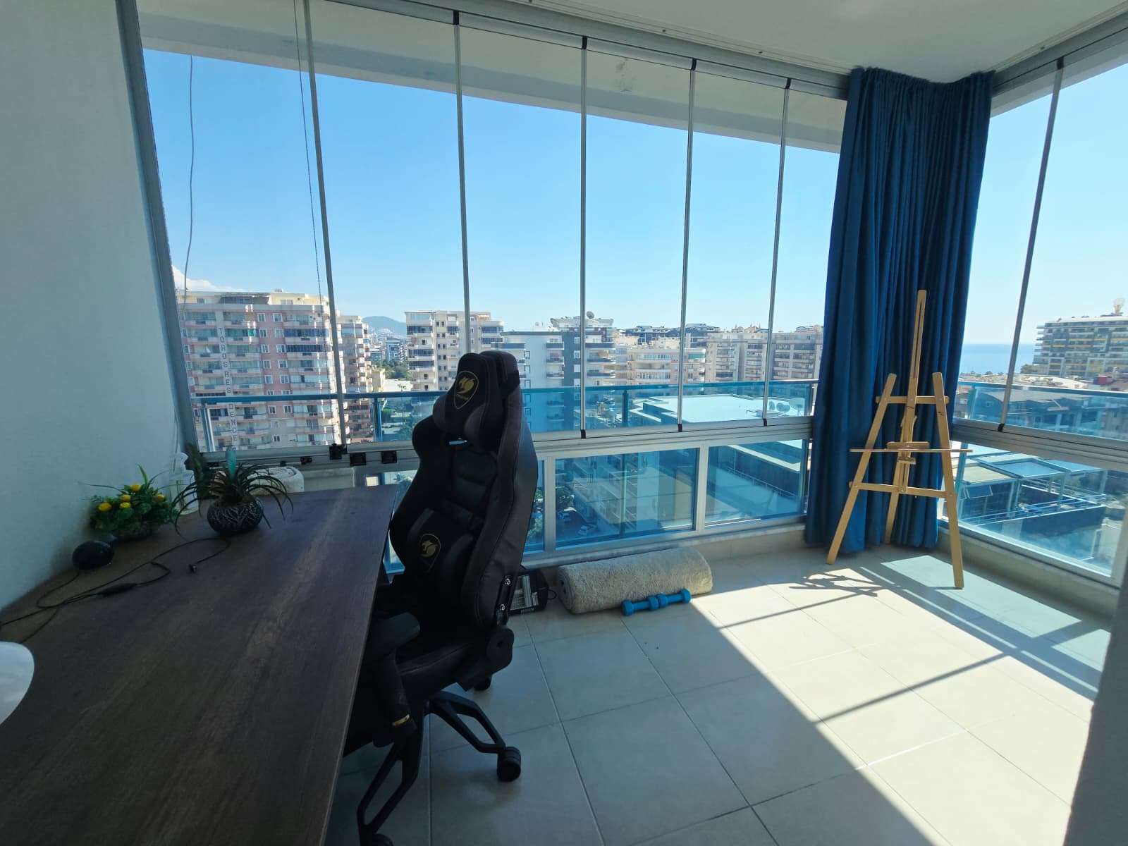Camlı köşe terasta çalışma masası, şehir manzarası ve şövale Mahmutlar’da satılık penthouse içinde