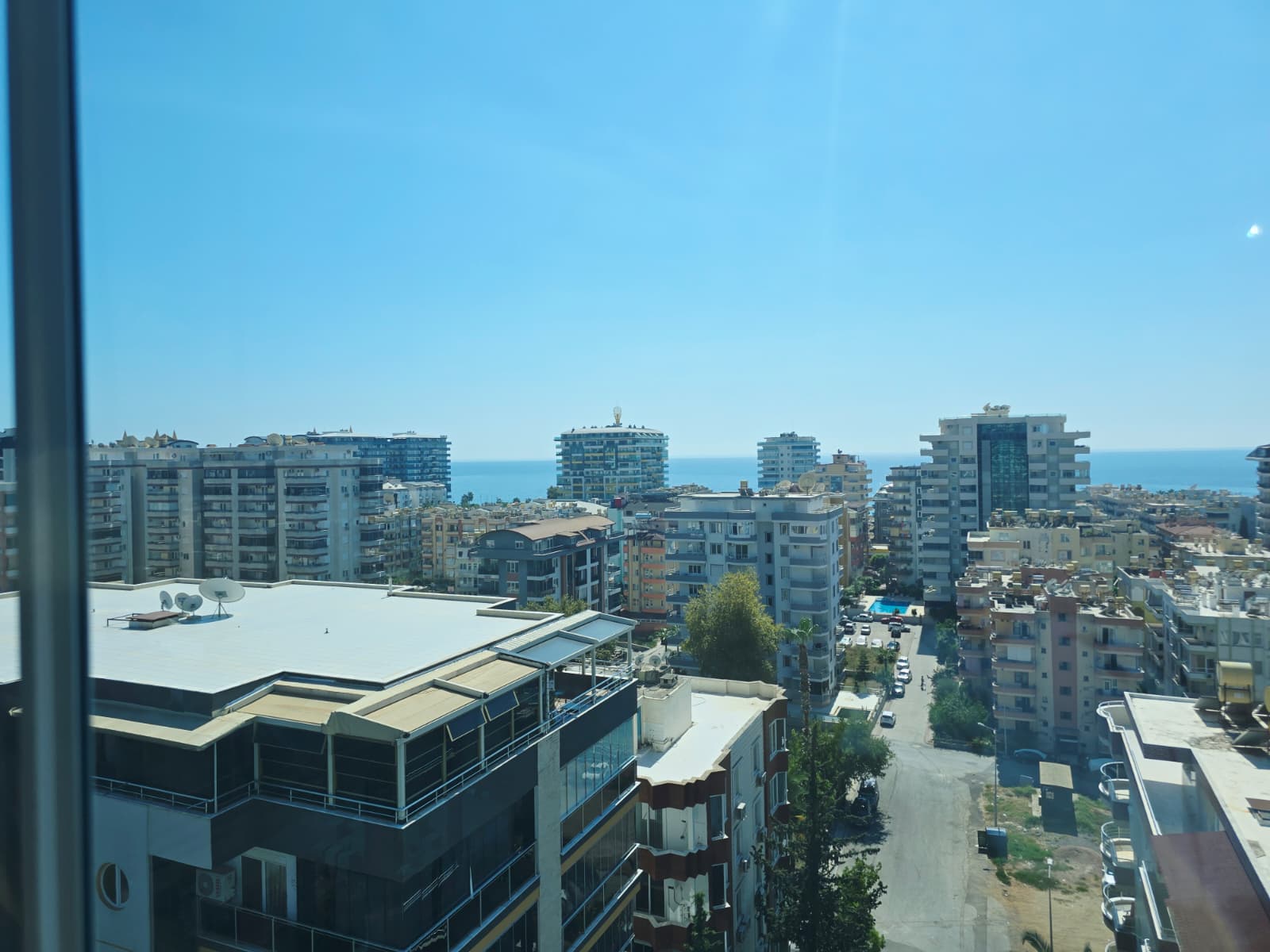Pencere arkasında yüksek konutlar, araçlar ve ufuktaki deniz satılık penthouse manzarasında