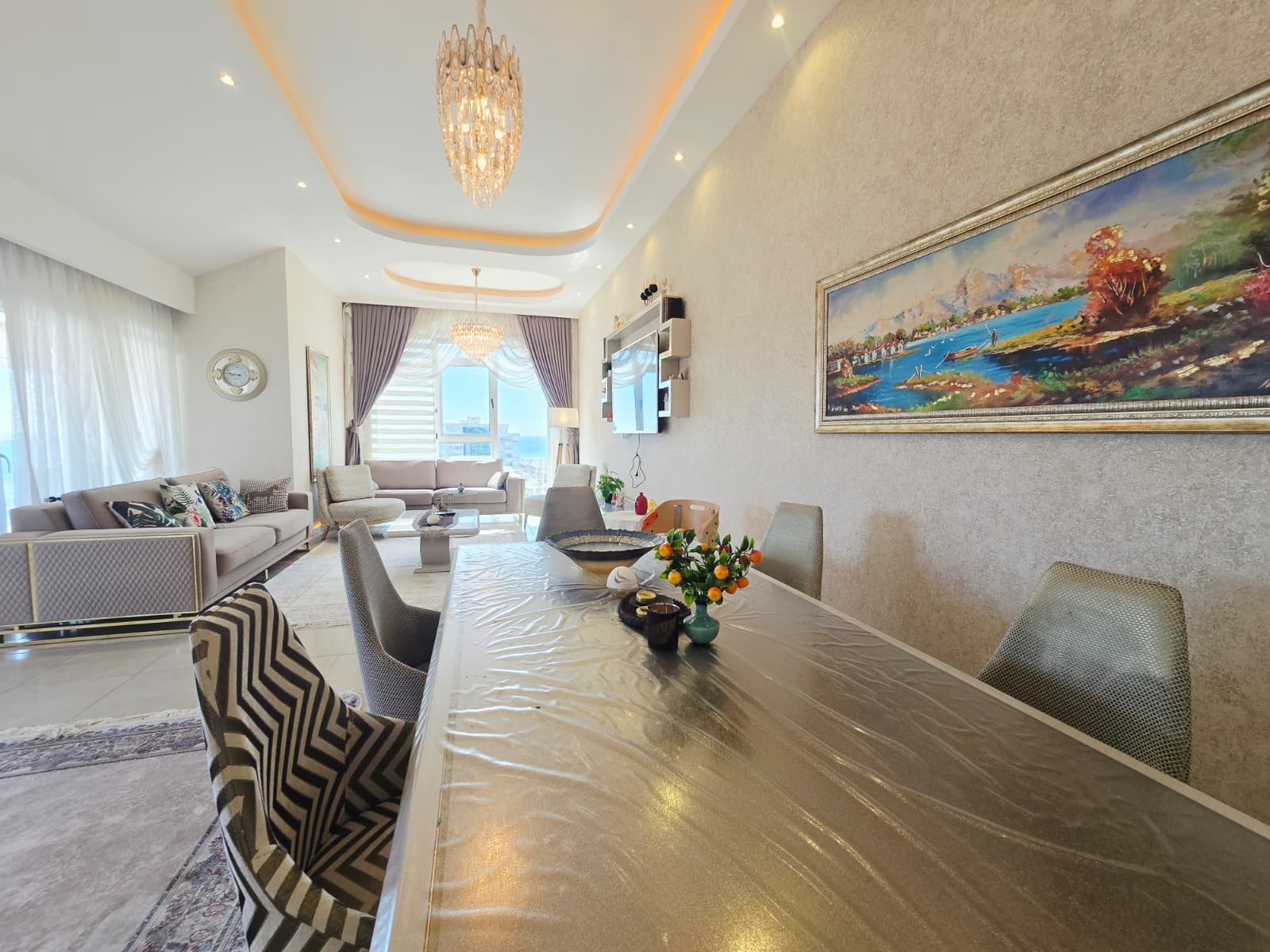 Yemek masası, açık renk kanepe ve perdeli panoramik pencere Mahmutlar’daki Türkiye rezidansında