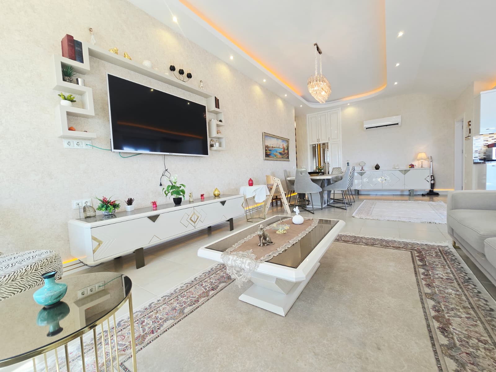 Duvar televizyonu, sehpa ve açık renk kanepe Mahmutlar’daki penthouse salonunda