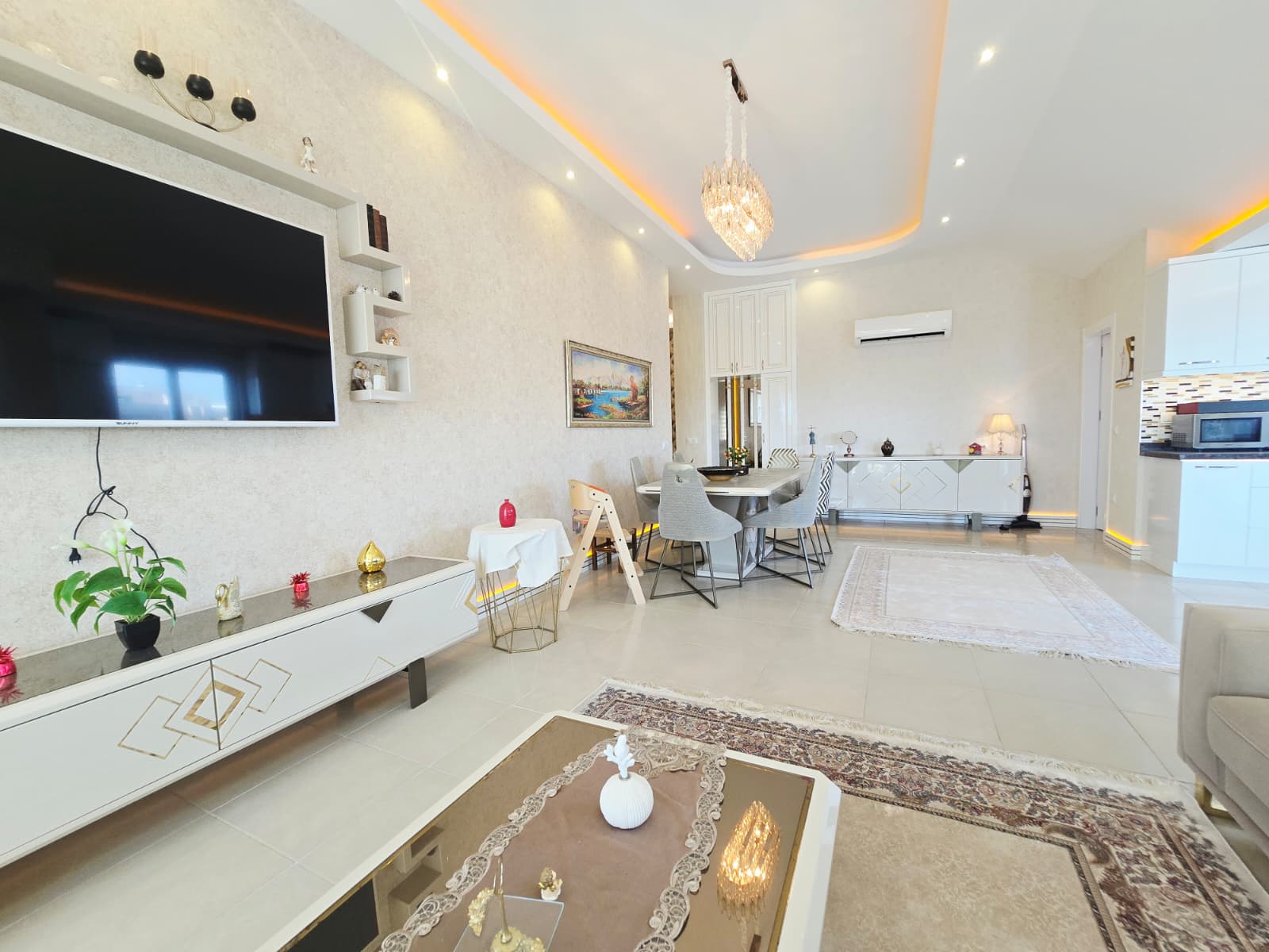 Büyük televizyon, beyaz ünite ve yemek alanı Türkiye’de satılık penthouse içinde