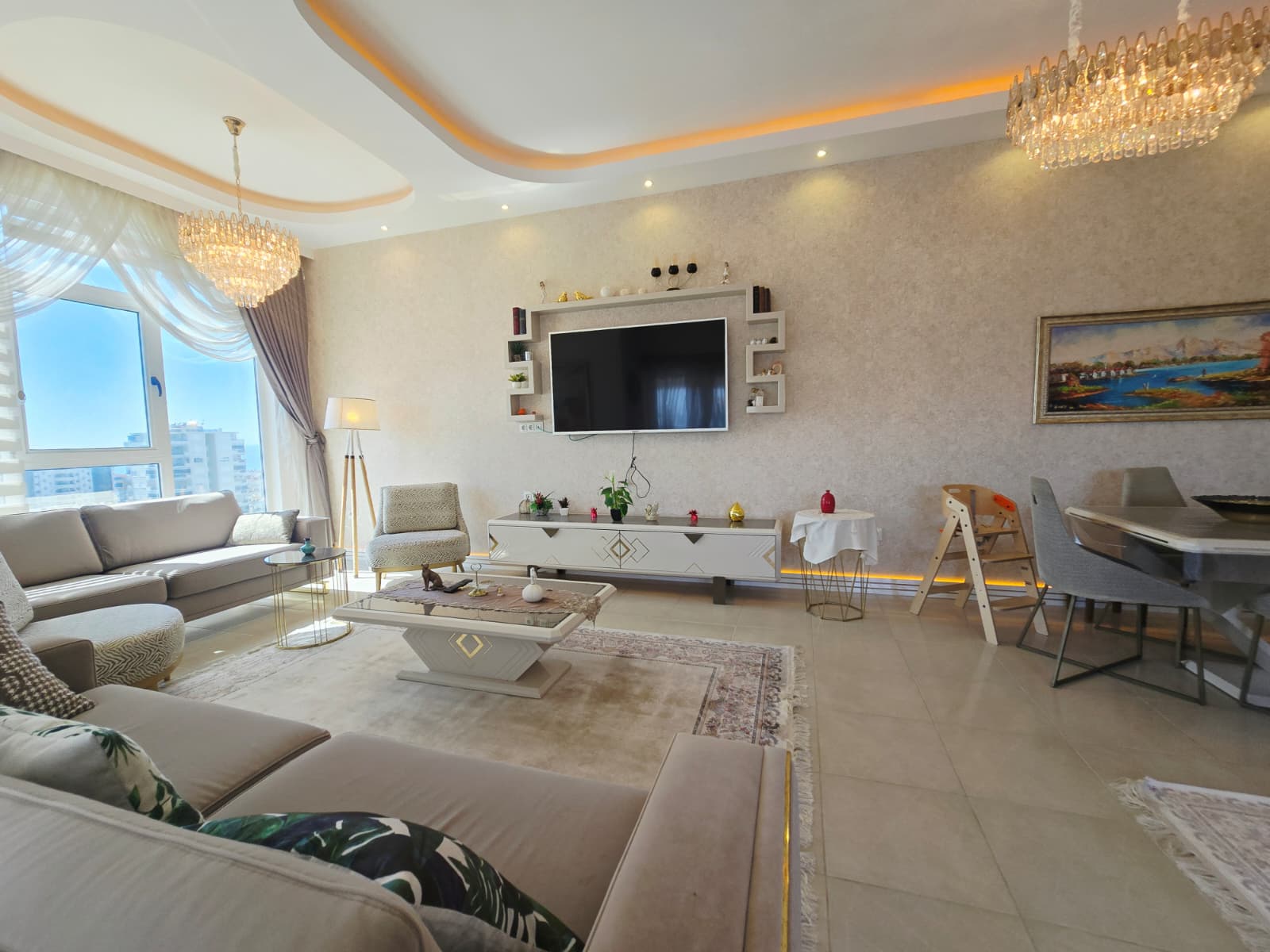 Açık renk kanepe, televizyon ve şehir manzaralı panoramik pencere Mahmutlar’da satılık dairede