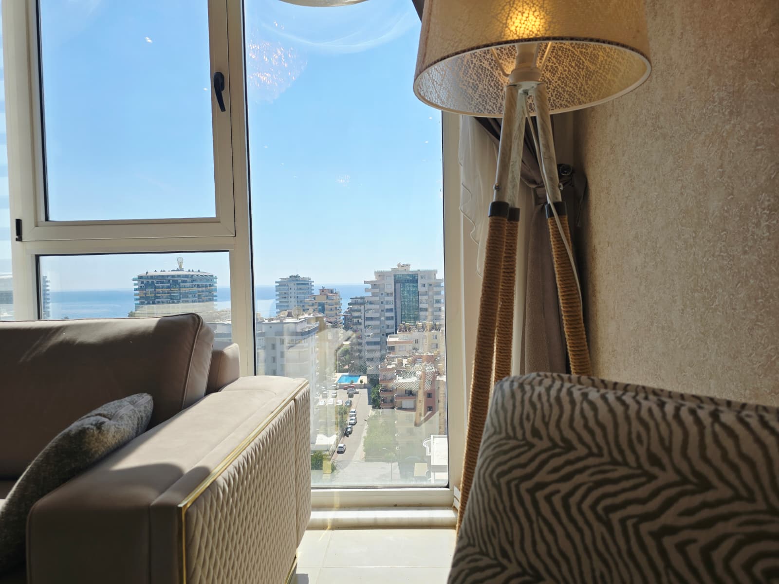Panoramik köşe penceresinden şehir ve deniz şeridi açık renk kanepenin yanında satılık dairede