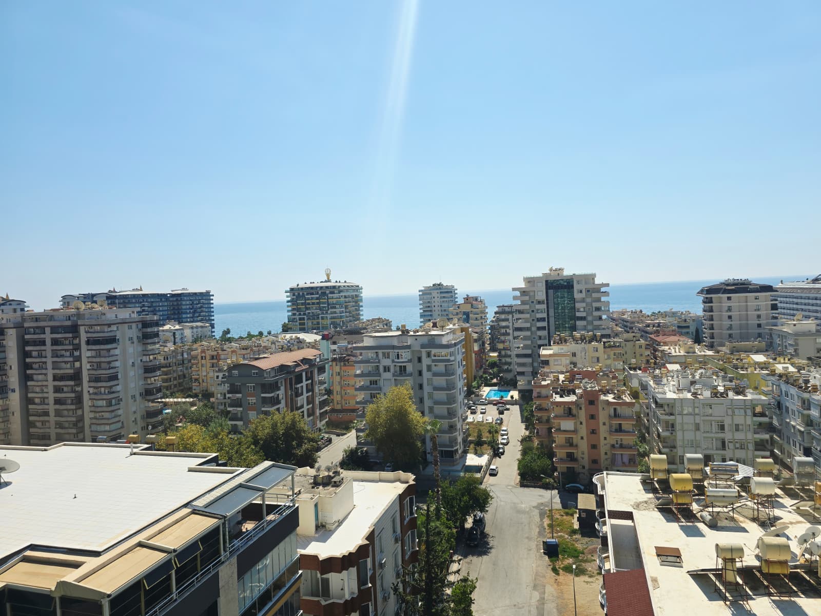 Mahmutlar’da yüksek binalar, arkadaki deniz ve park edilmiş araçlarla şehir manzarası