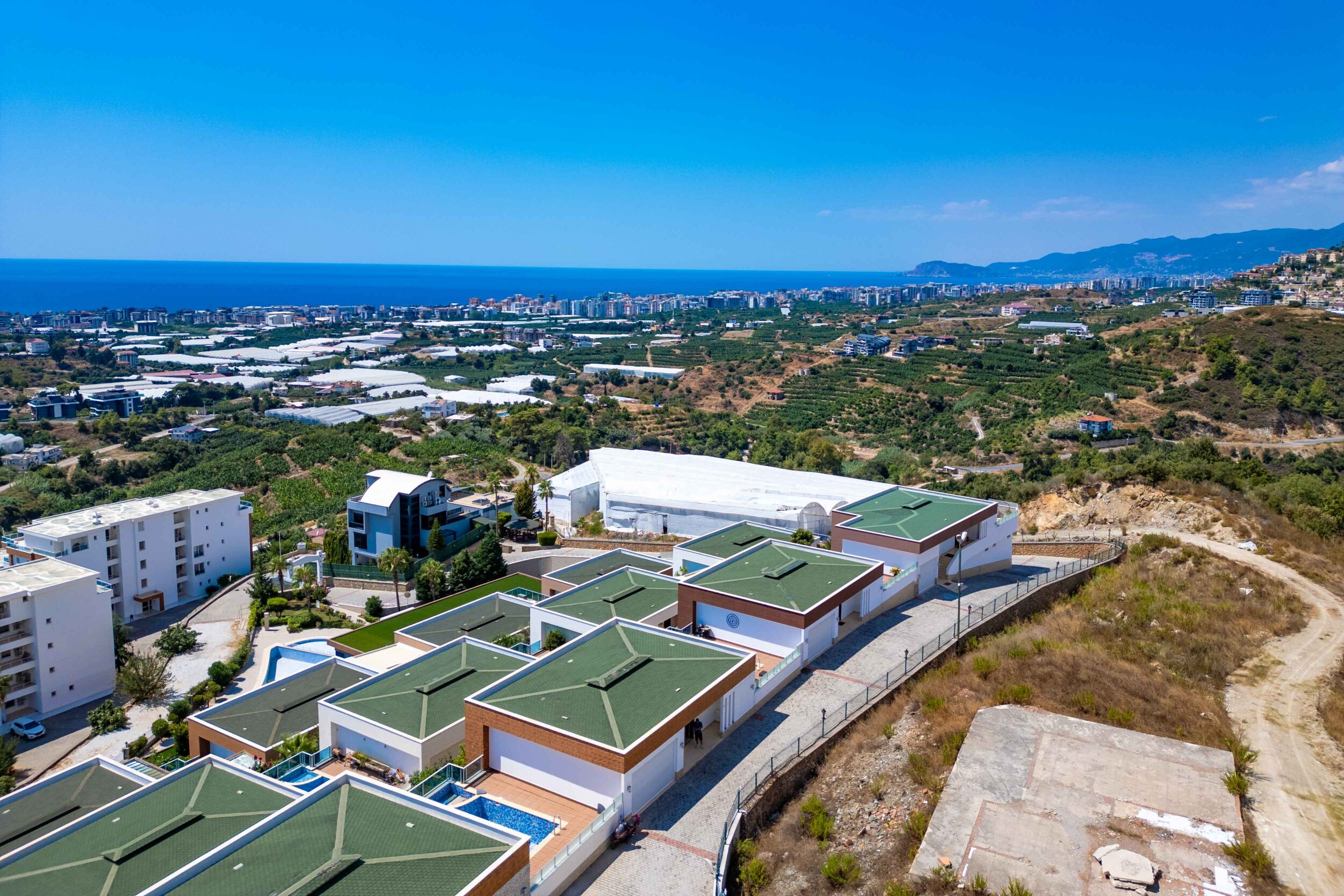 Villas with private pools and a paved road in Kargicak, Turkey with the coast and mountains beyond
