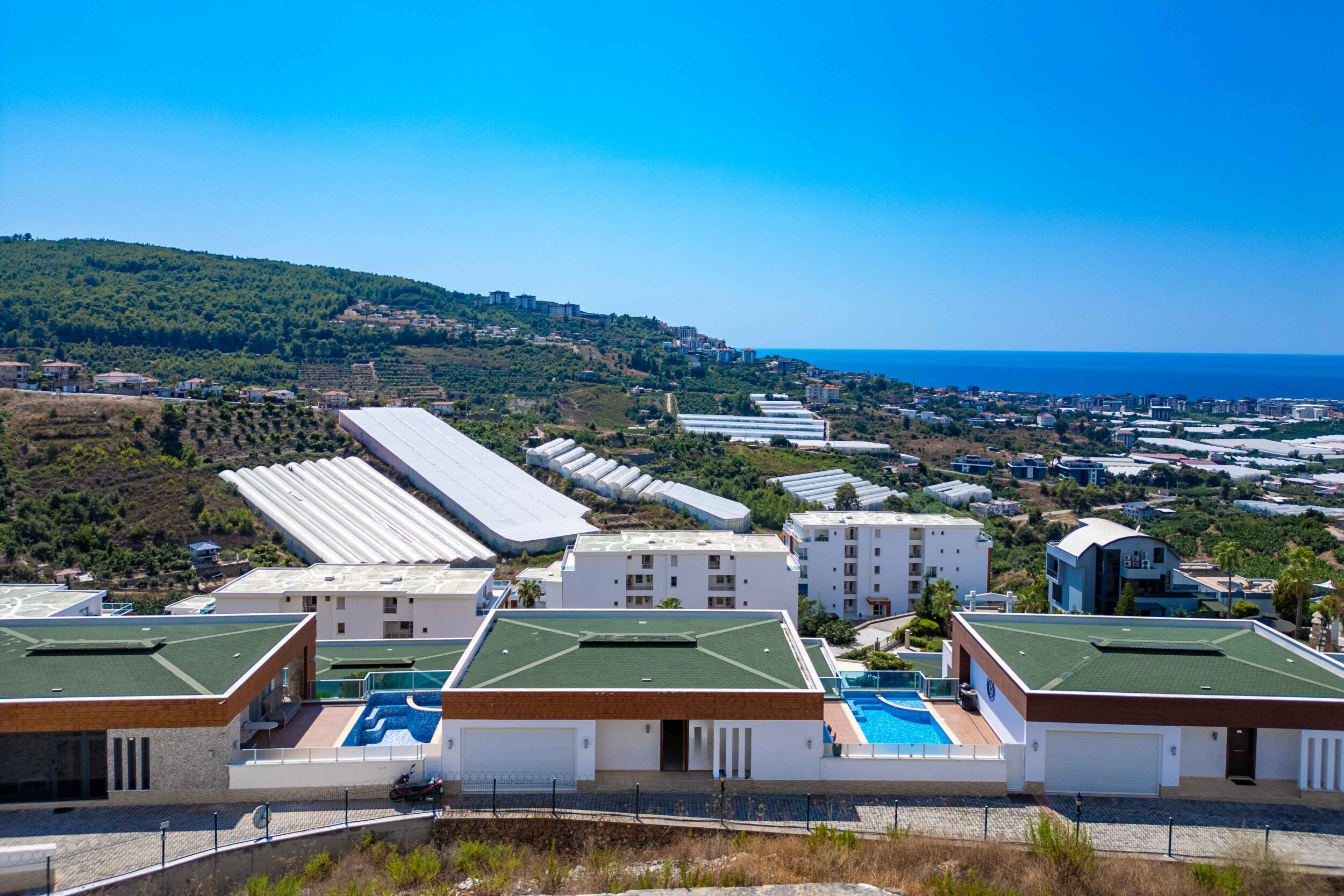 Villa facades with private pools and garage doors above the greenhouses in Kargicak