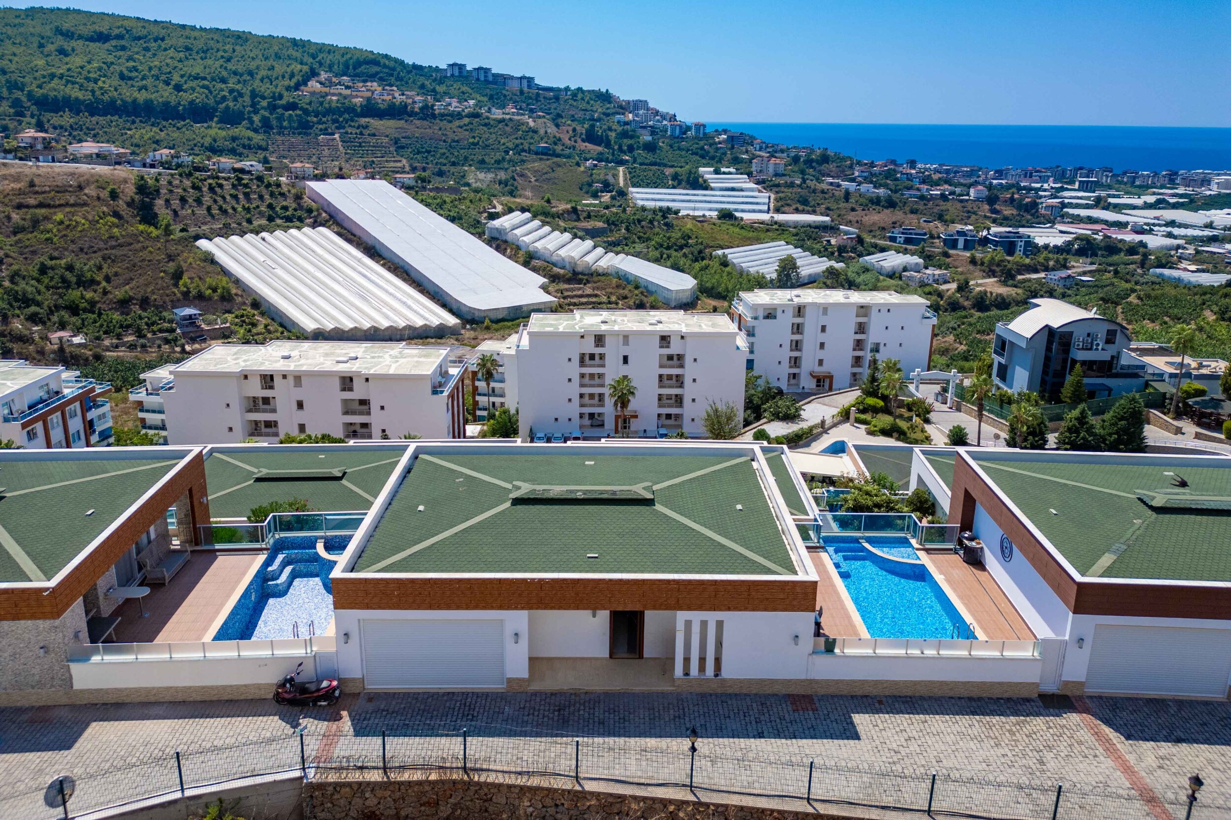 Aerial view of a villa for sale in Kargicak, centered between pools beneath a green roof